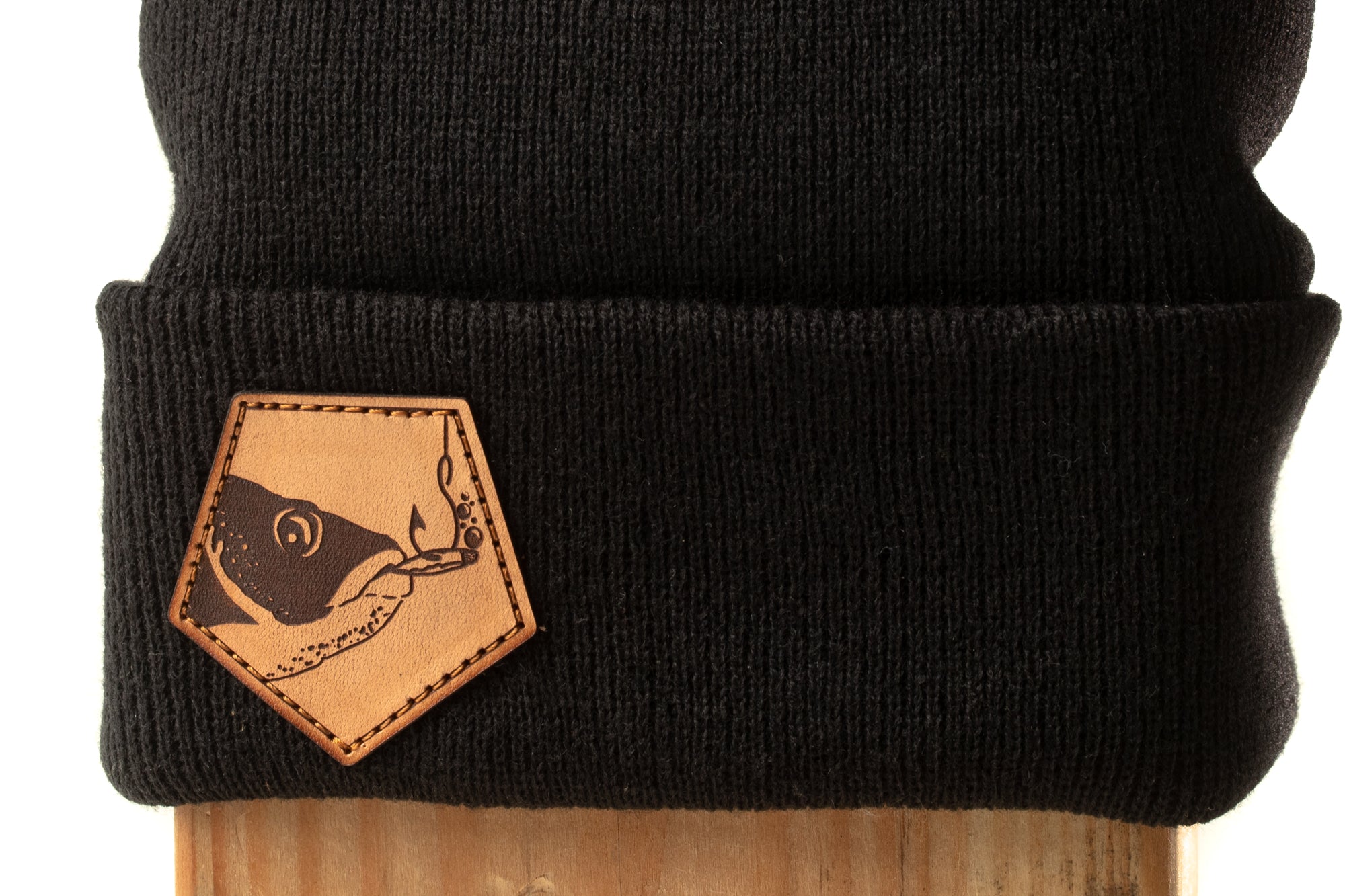A black knit cap with a leather patch featuring a fish design.