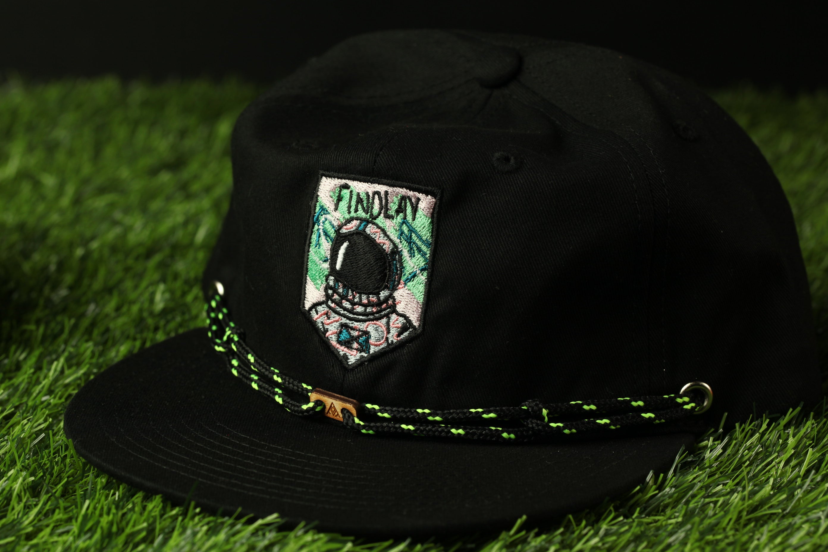 A black baseball cap with a green and white embroidered patch on the front, featuring a graphic of a person wearing a helmet and the word "FINDOLAY" written on it.