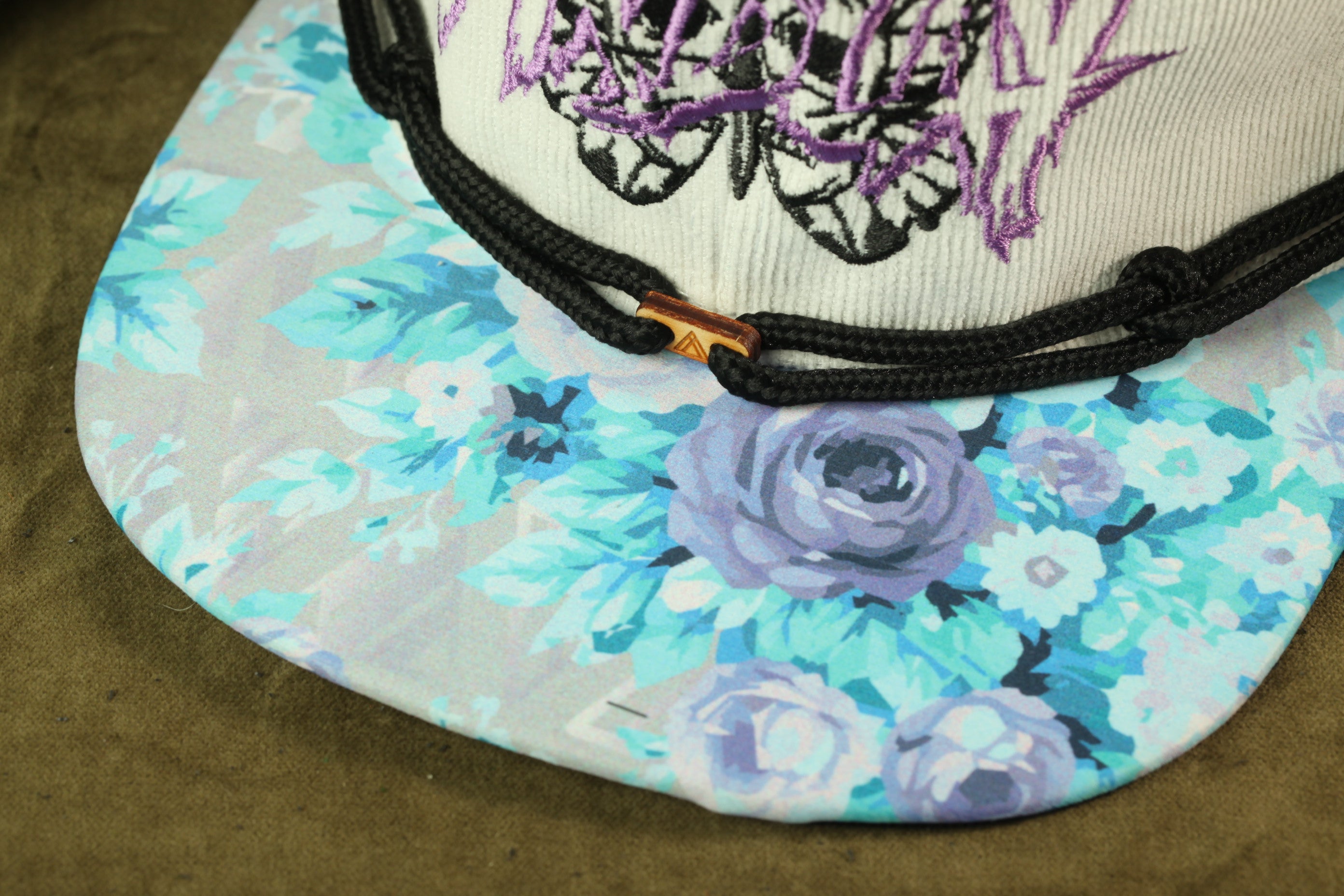 A close-up view of a floral patterned baseball cap with a black lace detail and a purple butterfly design.
