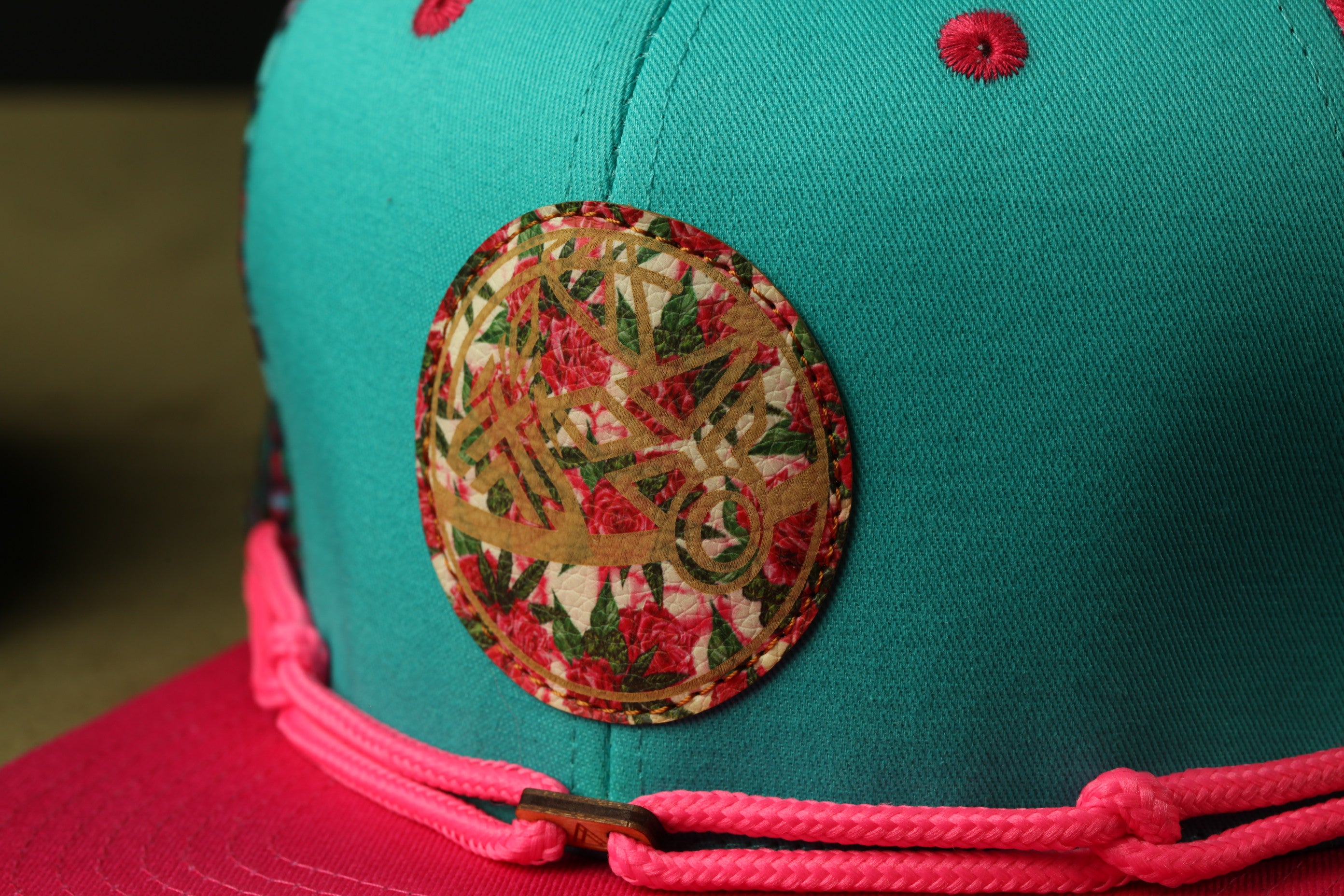 A close-up view of a turquoise baseball cap with a red and pink decorative element on the front.