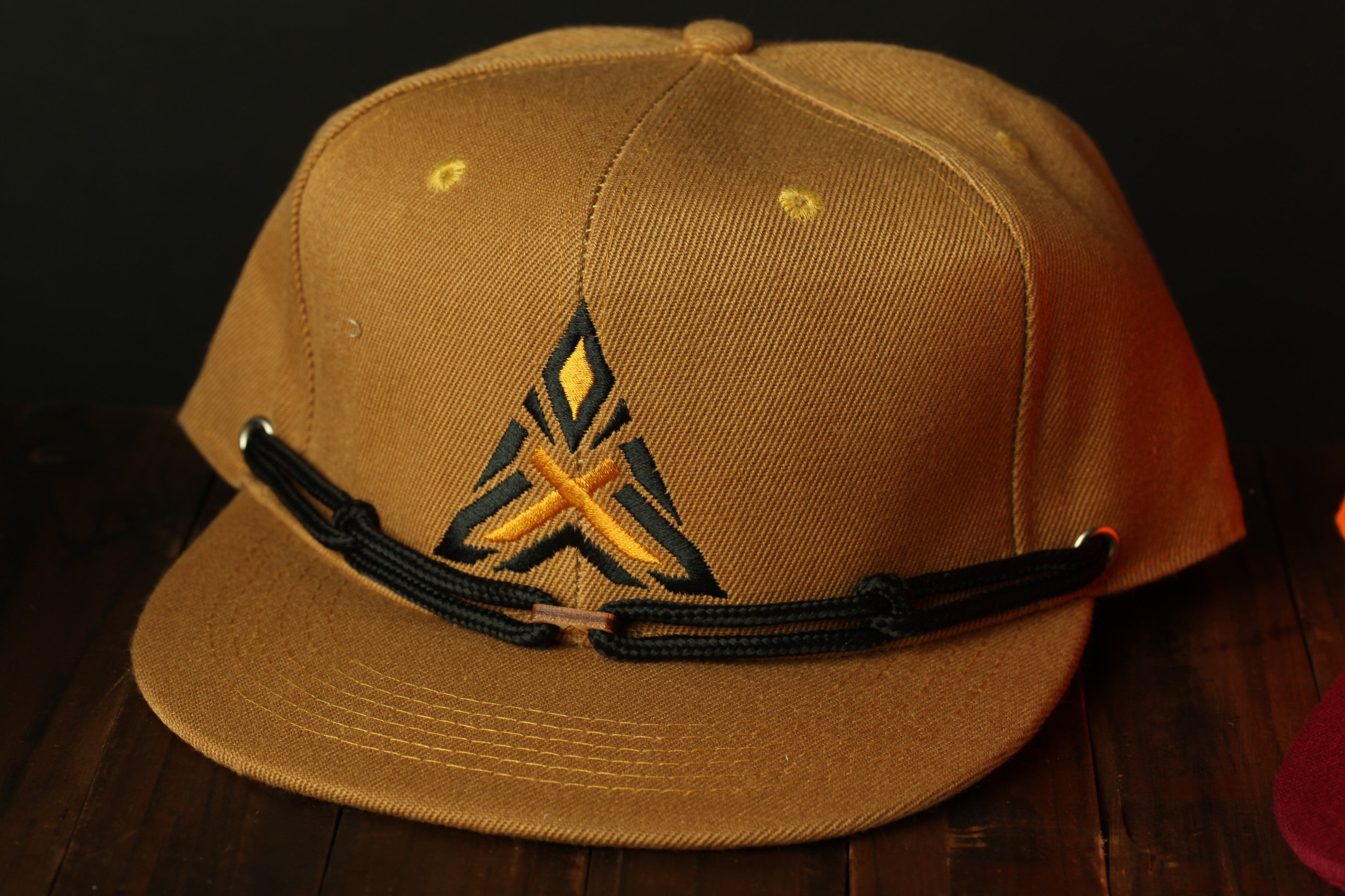 A tan baseball cap with a black and yellow embroidered logo on the front, sitting on a wooden surface.