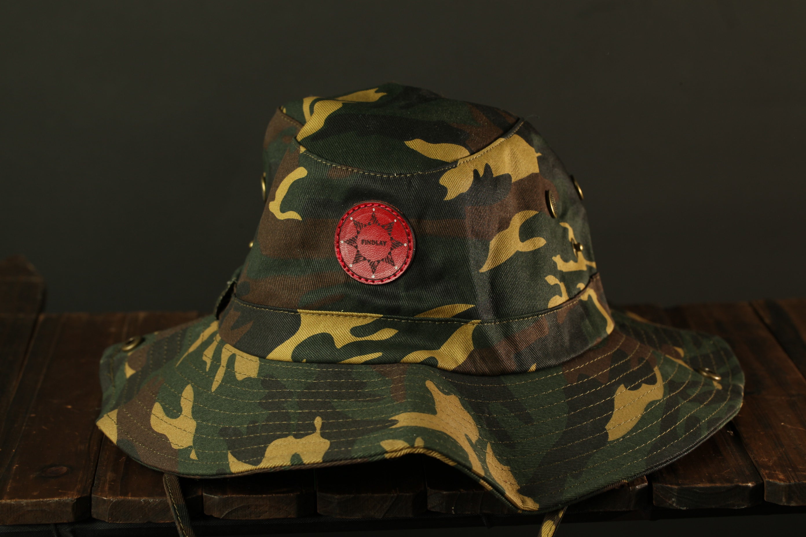 A camouflage military-style hat with a red star patch on the front, placed on a wooden surface.