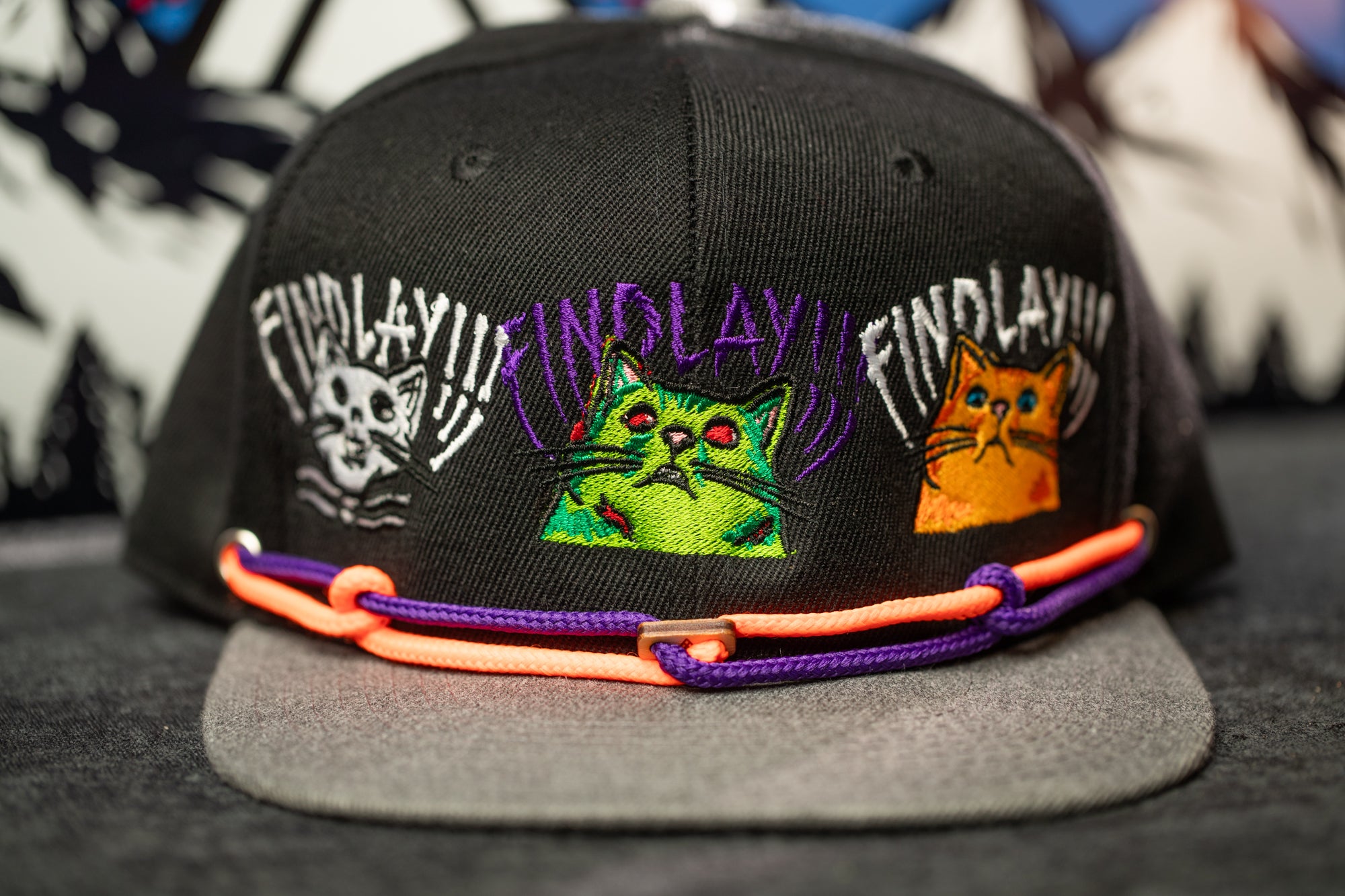A black baseball cap with colorful cat designs and the text "FIND LAY" printed on it.
