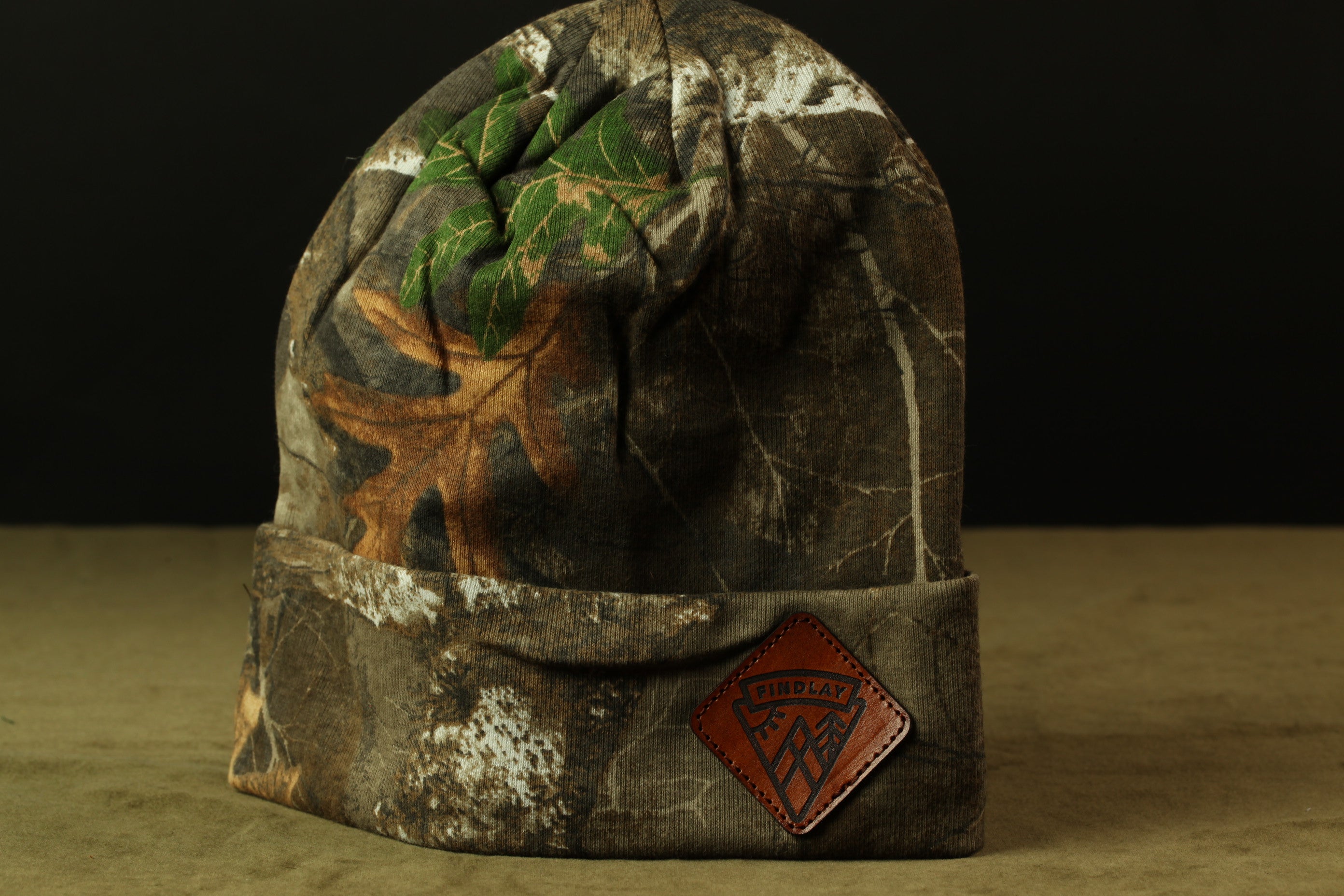 A camouflage-patterned beanie with a patch on the front displaying the text "FIND LAY".