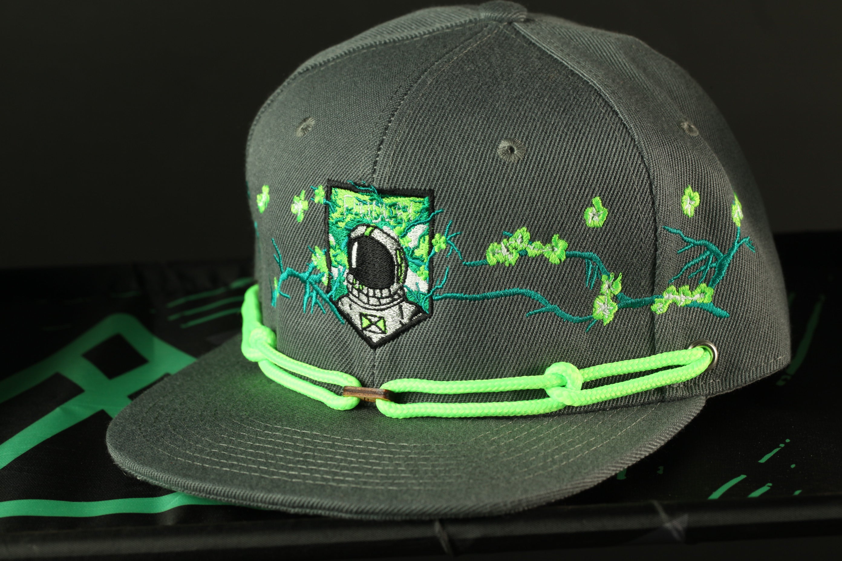 A gray baseball cap with a green strap and a small, green-colored emblem on the front.