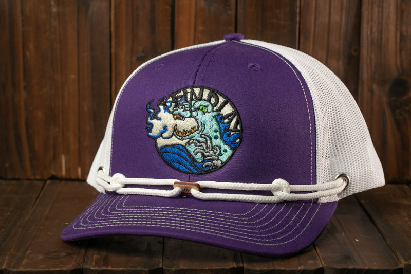 A purple baseball cap with a white mesh panel and a circular embroidered logo on the front, sitting on a wooden surface.