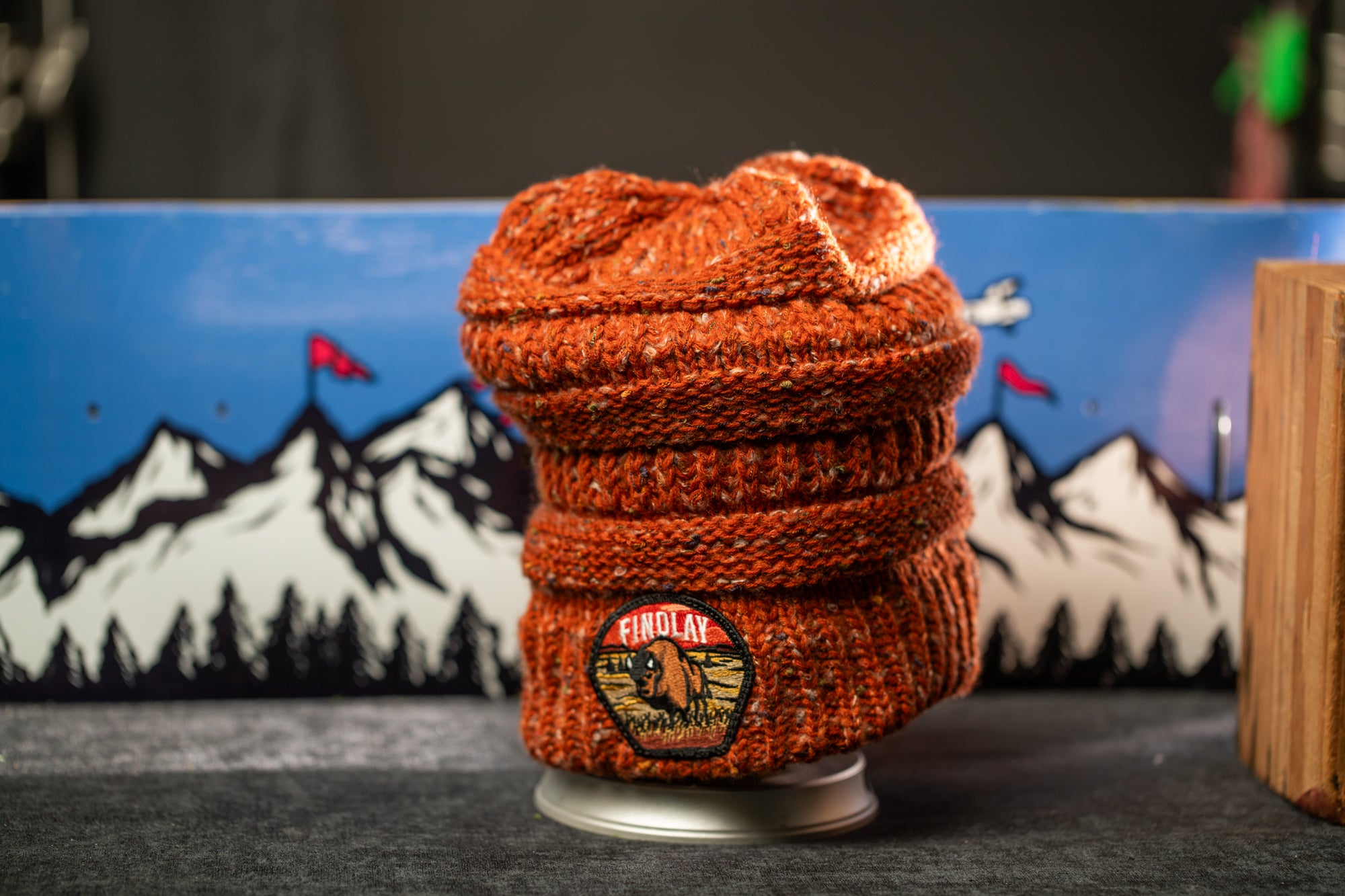 A knitted orange beanie with a mountain landscape design on the front, placed on a gray surface.
