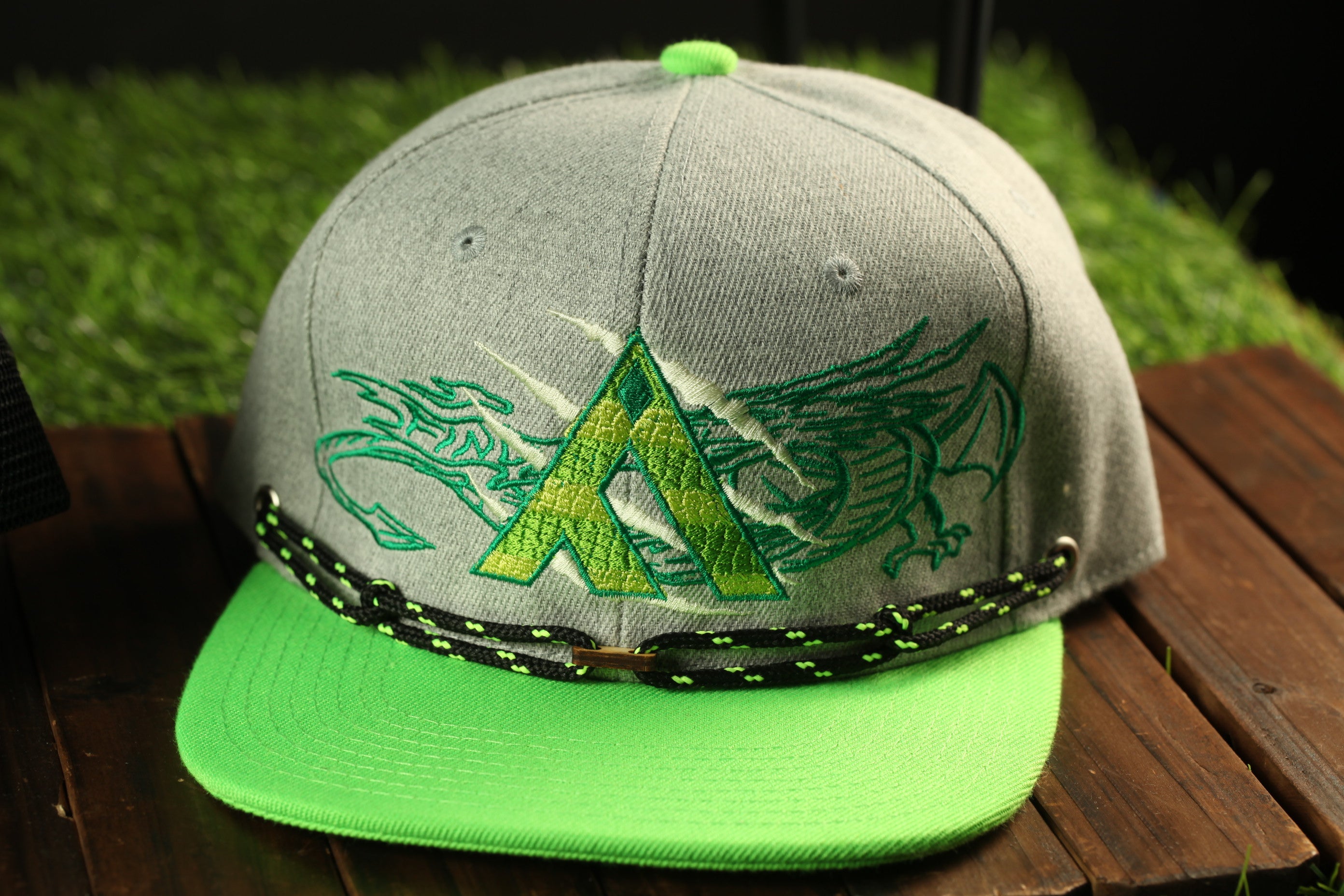 A gray baseball cap with a green and black design featuring a stylized letter 'A' and a dragon-like creature.