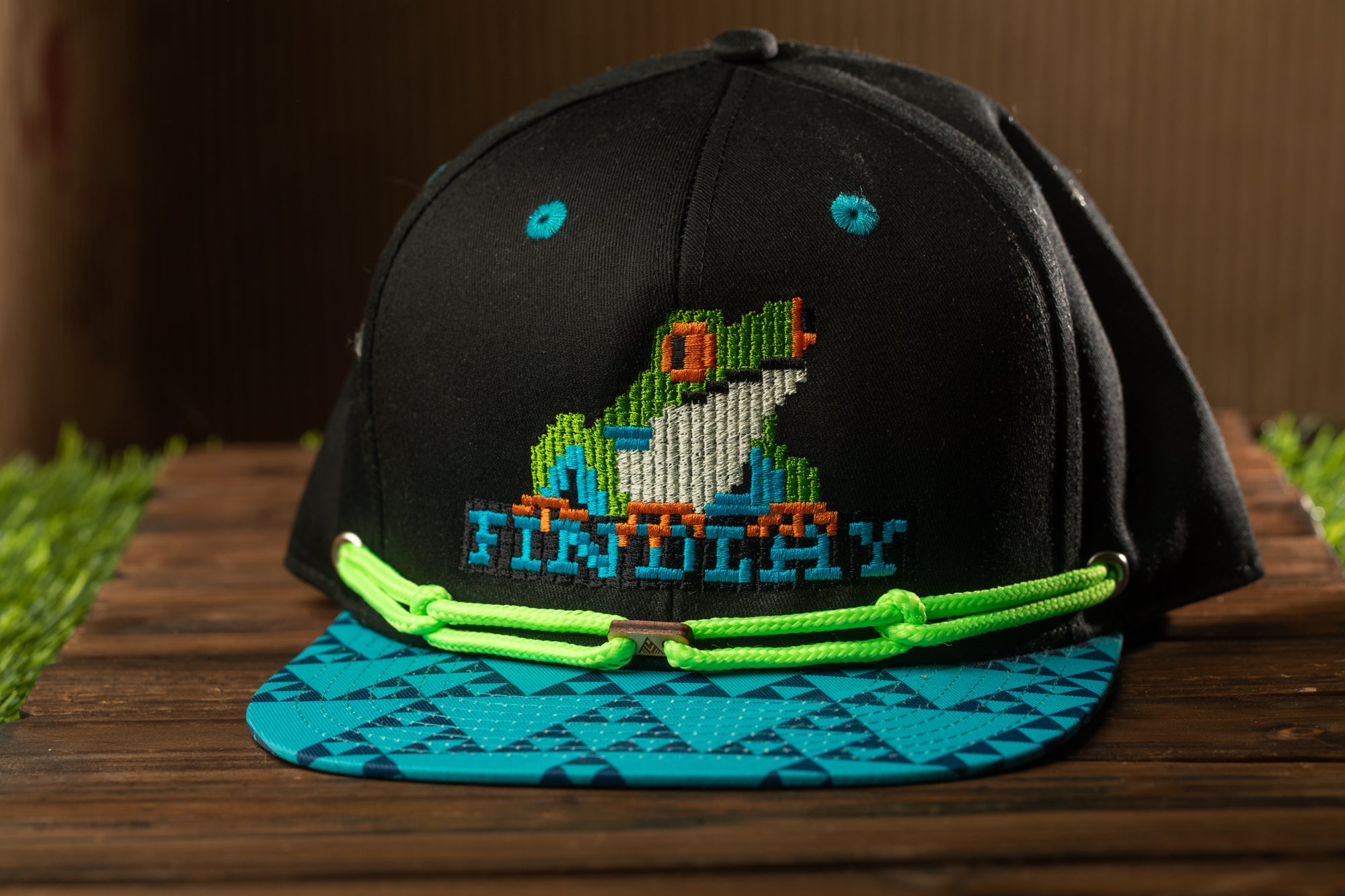 A black baseball cap with a colorful frog design and the word "FINCHY" printed on it, sitting on a wooden surface.