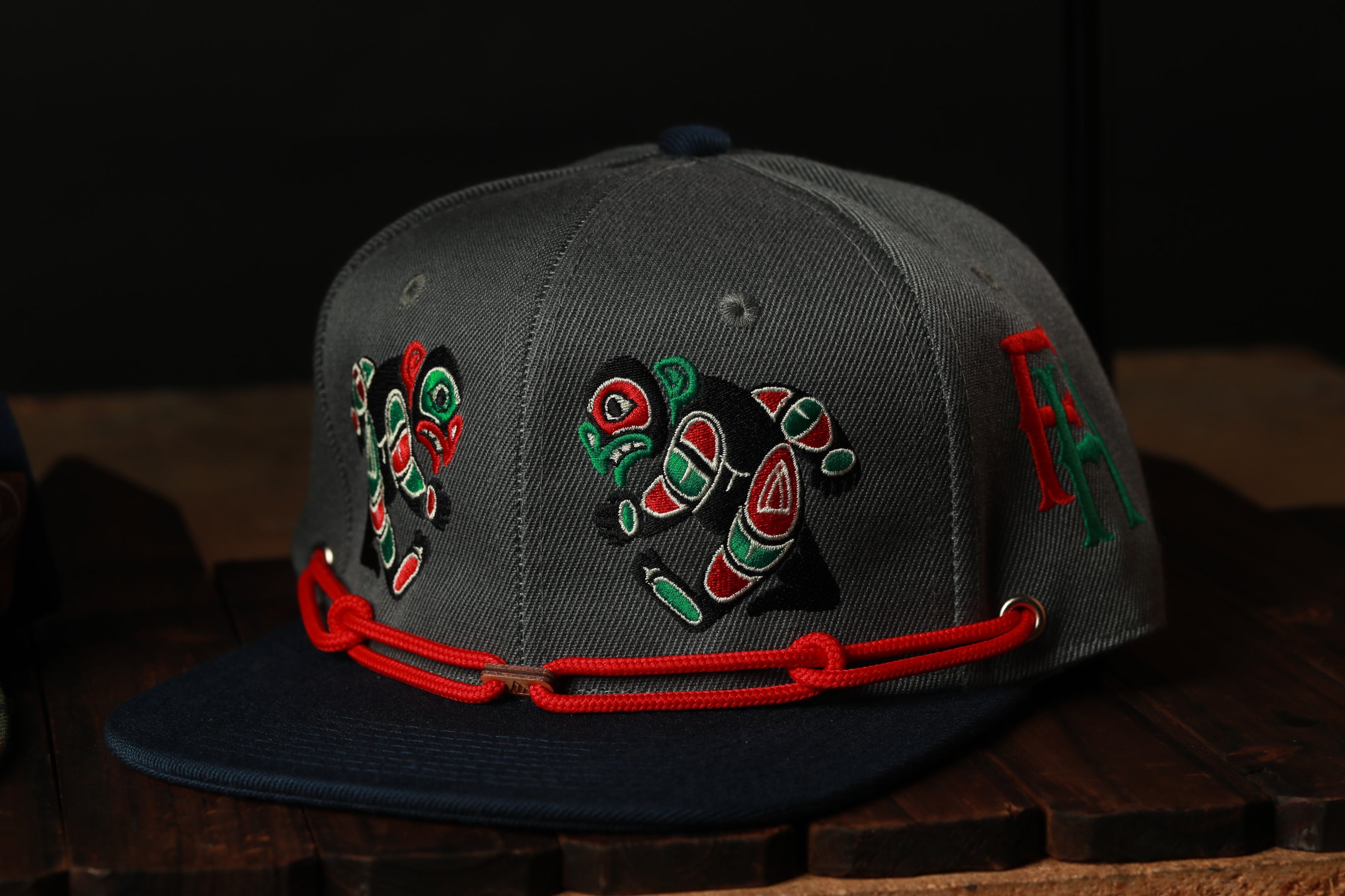 A gray baseball cap with red and green embroidered designs on the front, sitting on a wooden surface.