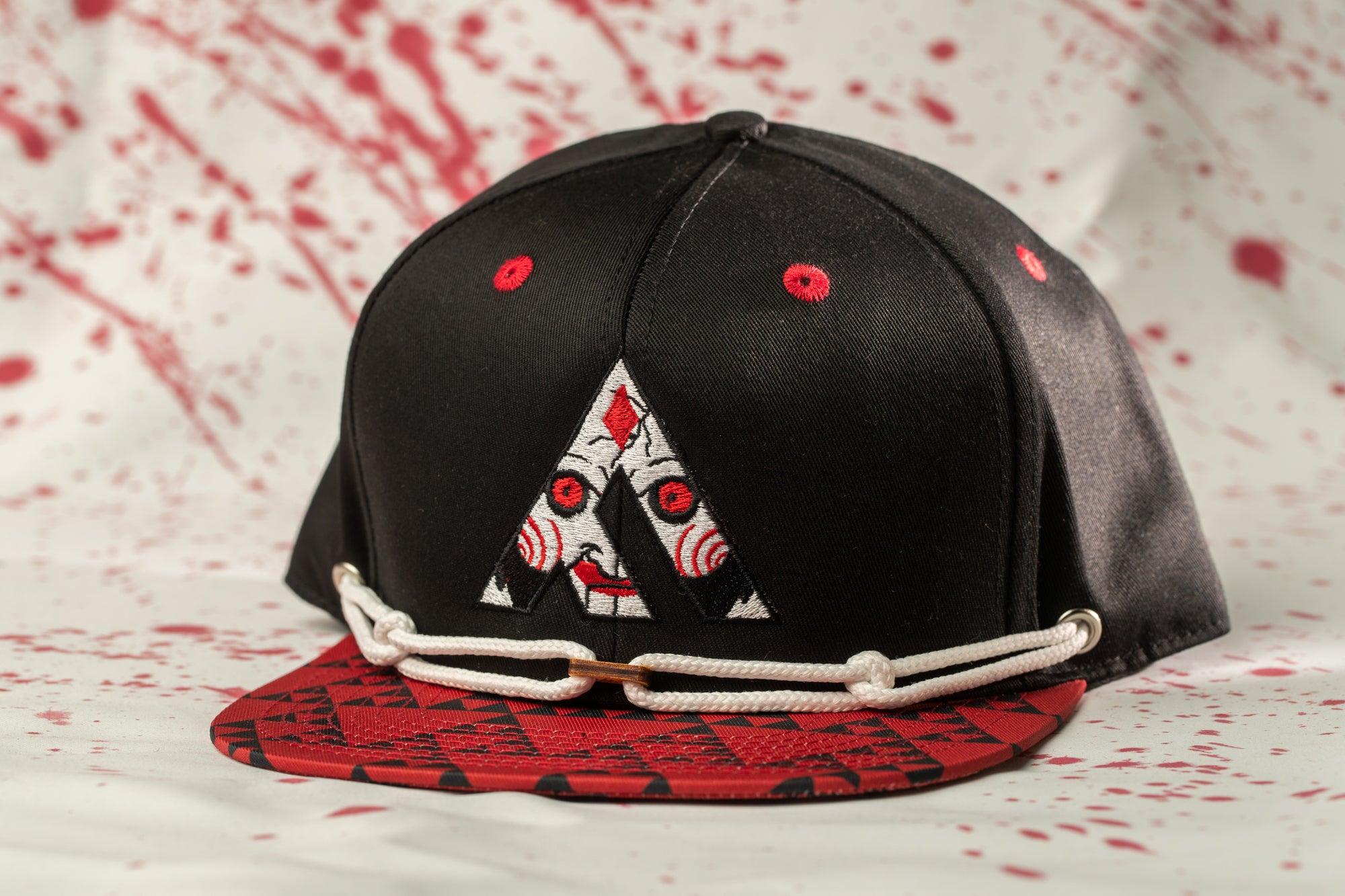 A black baseball cap with a red and white design on the front, featuring a stylized letter 'A' and a red dot on the brim.