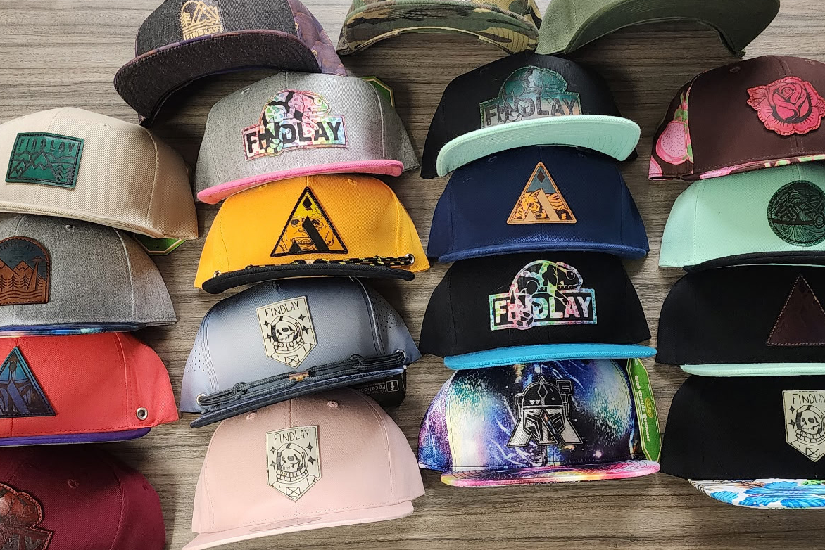 A collection of various colorful baseball caps and hats, including some with unique designs and logos, displayed on a wooden surface.
