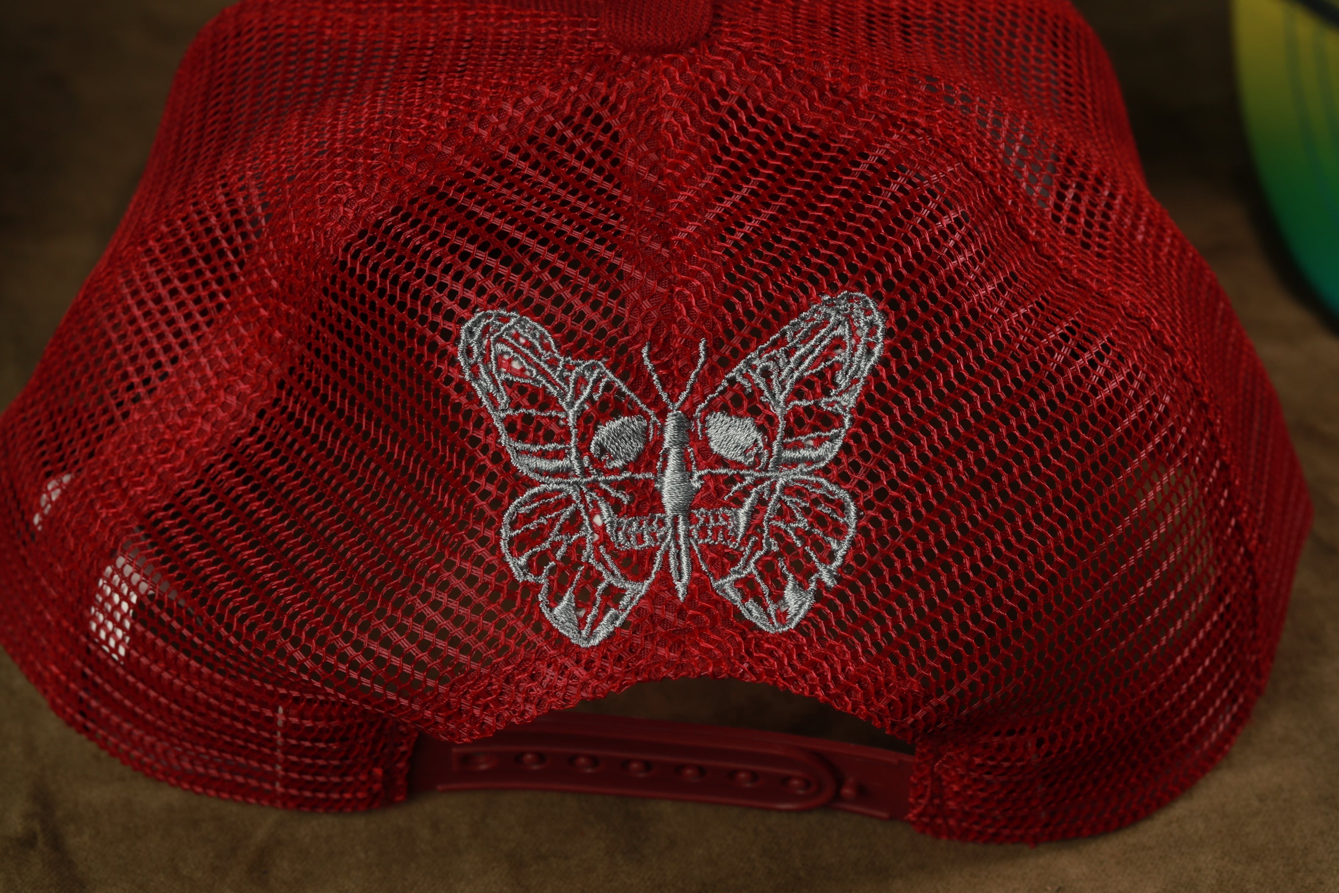 A close-up view of a red mesh hat with a silver butterfly design on the front.