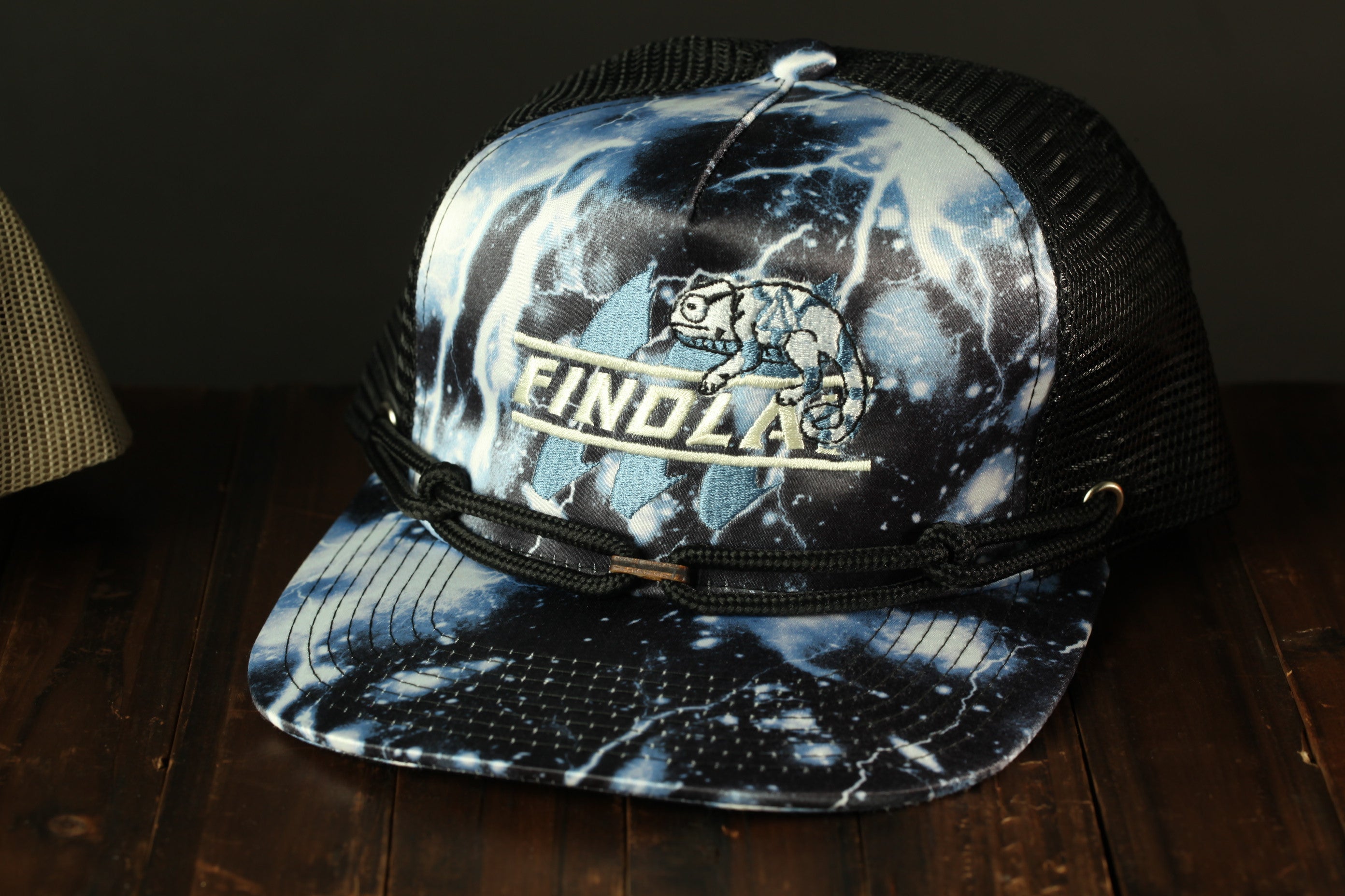A black and white baseball cap with a tie-dye pattern and the word "FINDOL" printed on it, sitting on a wooden surface.