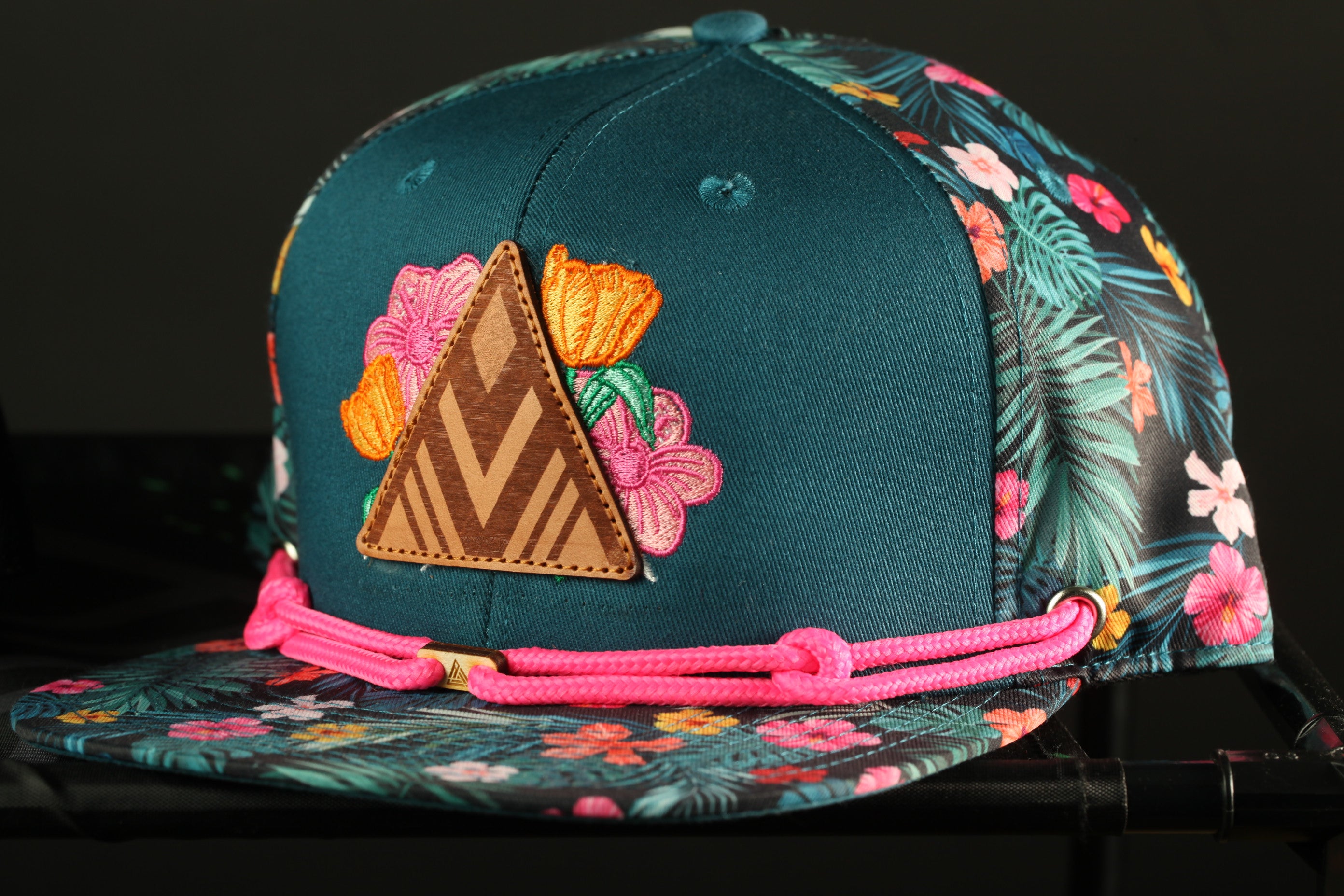 A colorful floral-patterned baseball cap with a triangular patch and pink braided straps.