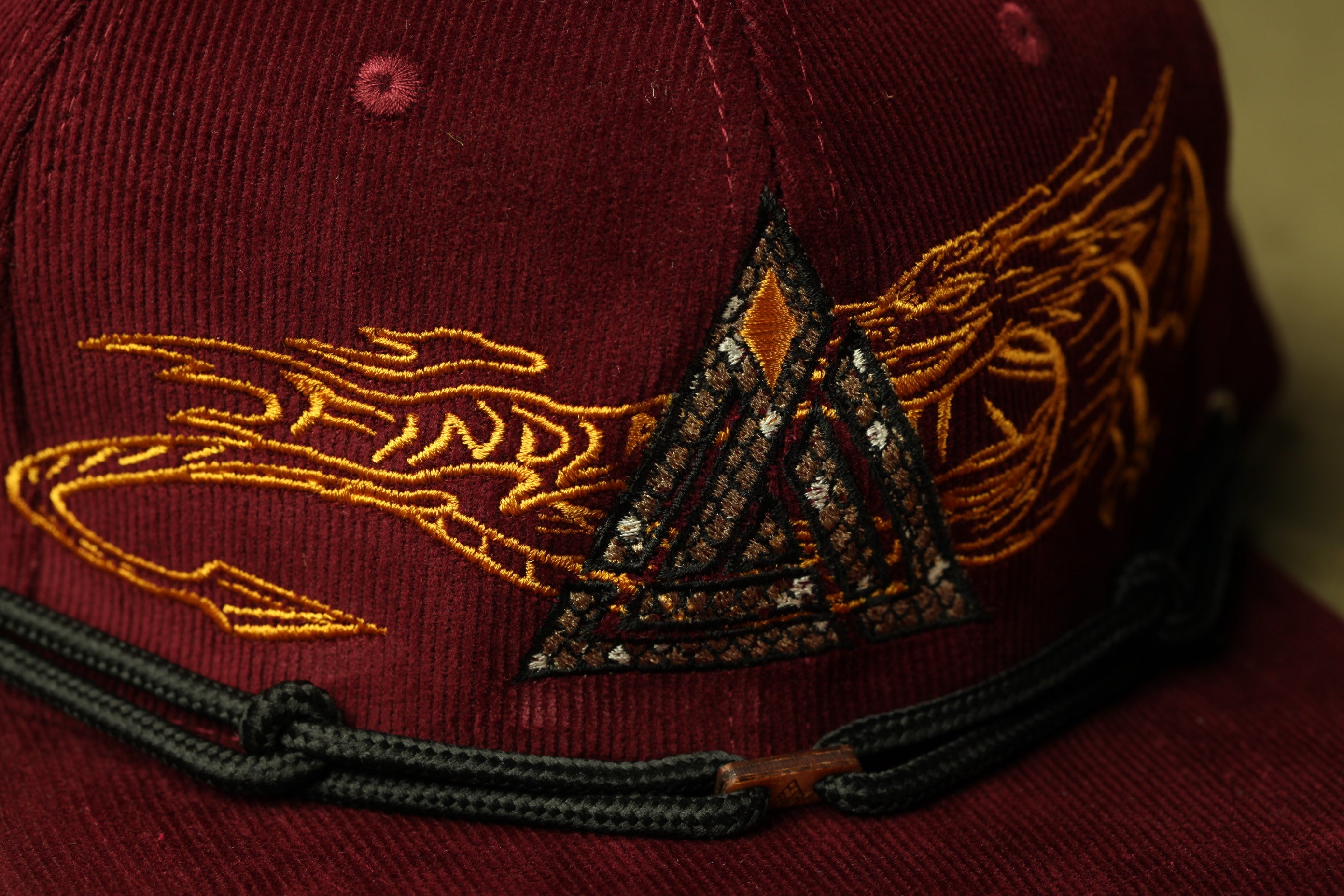A close-up view of a burgundy baseball cap with a gold dragon embroidered on it.