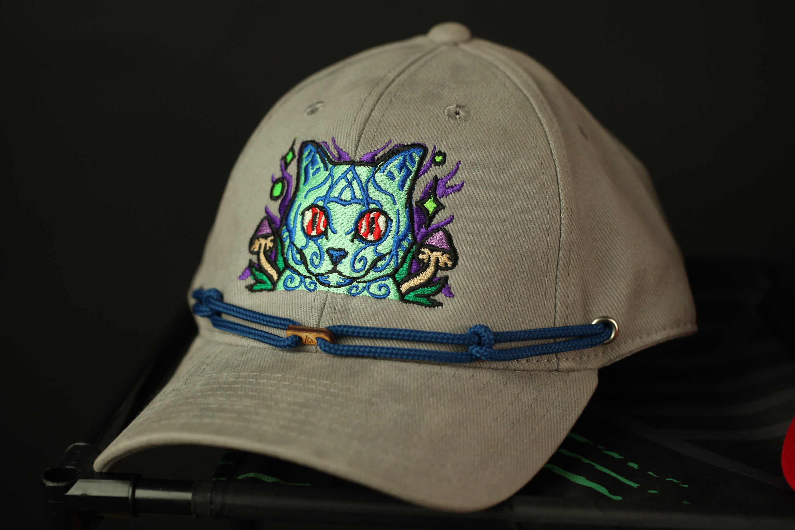 A beige baseball cap with a colorful, embroidered cat design on the front.