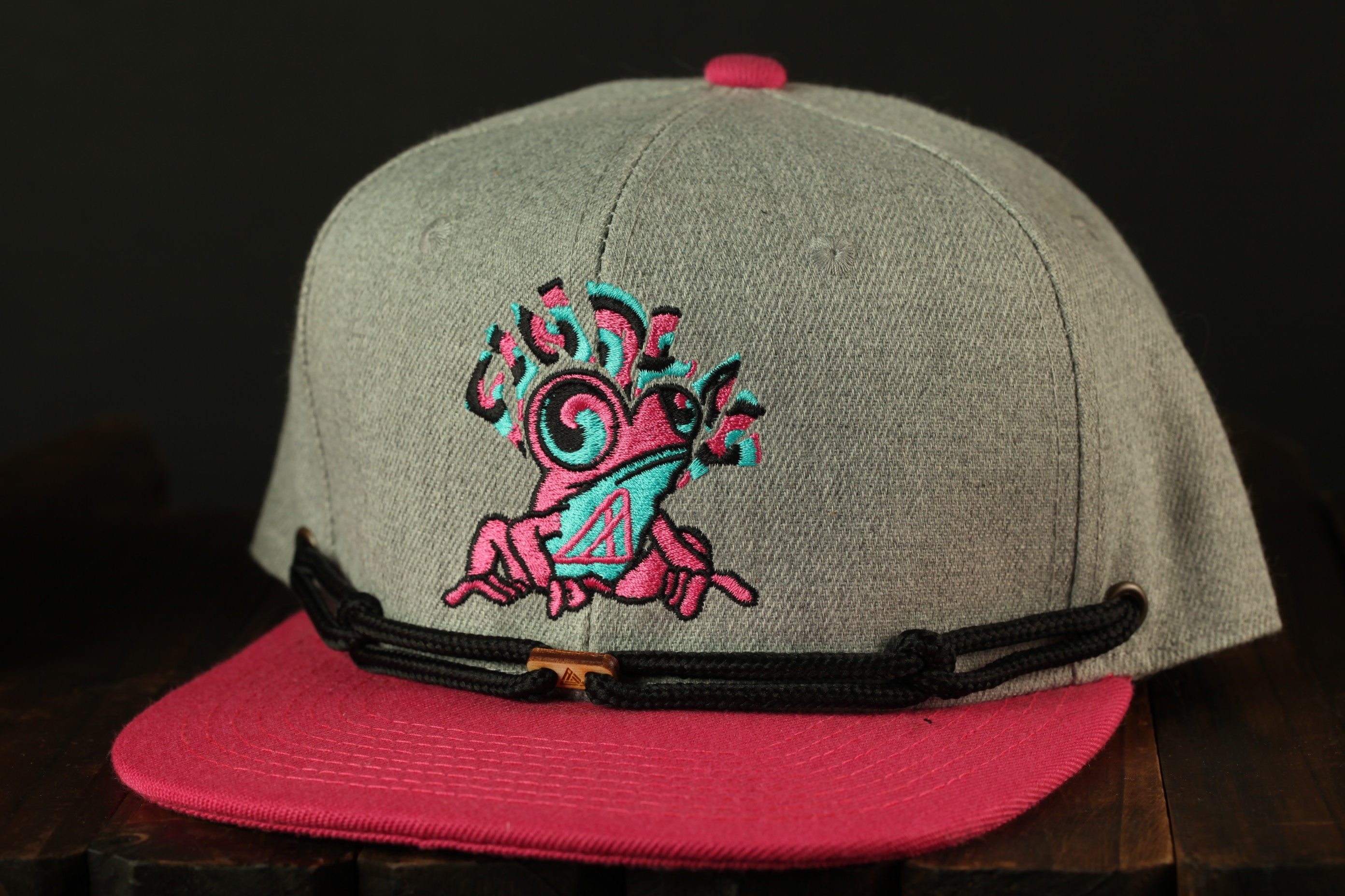 A gray baseball cap with a pink brim and a black strap, featuring a colorful, abstract design on the front.