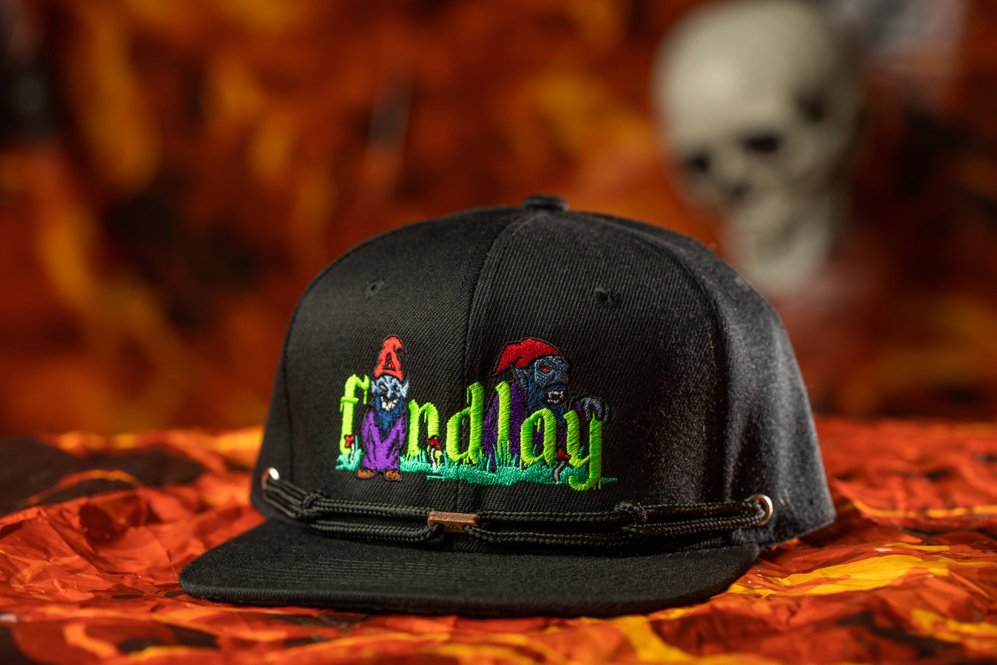 A black baseball cap with colorful embroidered characters on it, placed on a red and orange background.