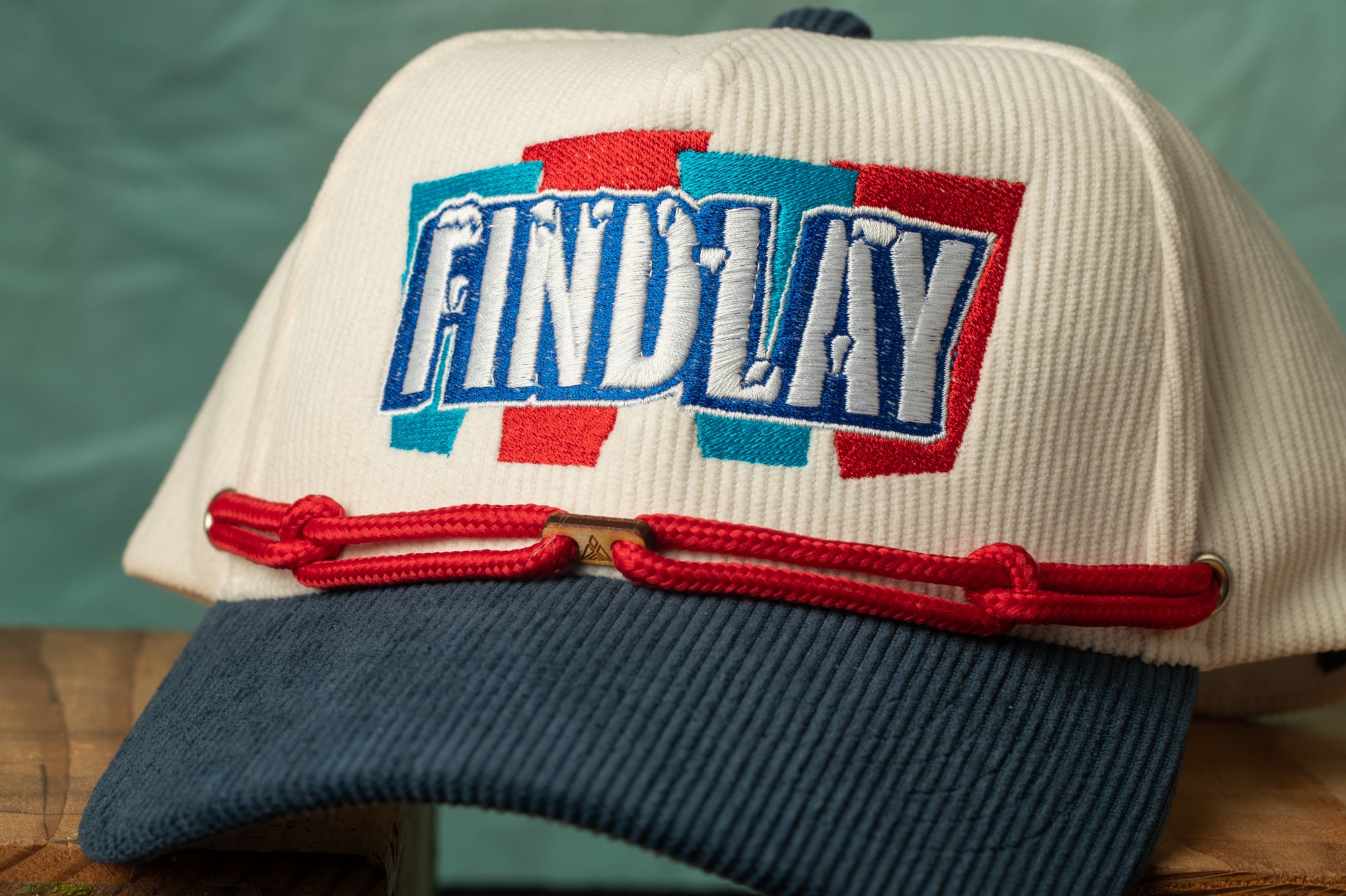 A white baseball cap with the word "FIND LAY" embroidered on it, along with a red string or ribbon.