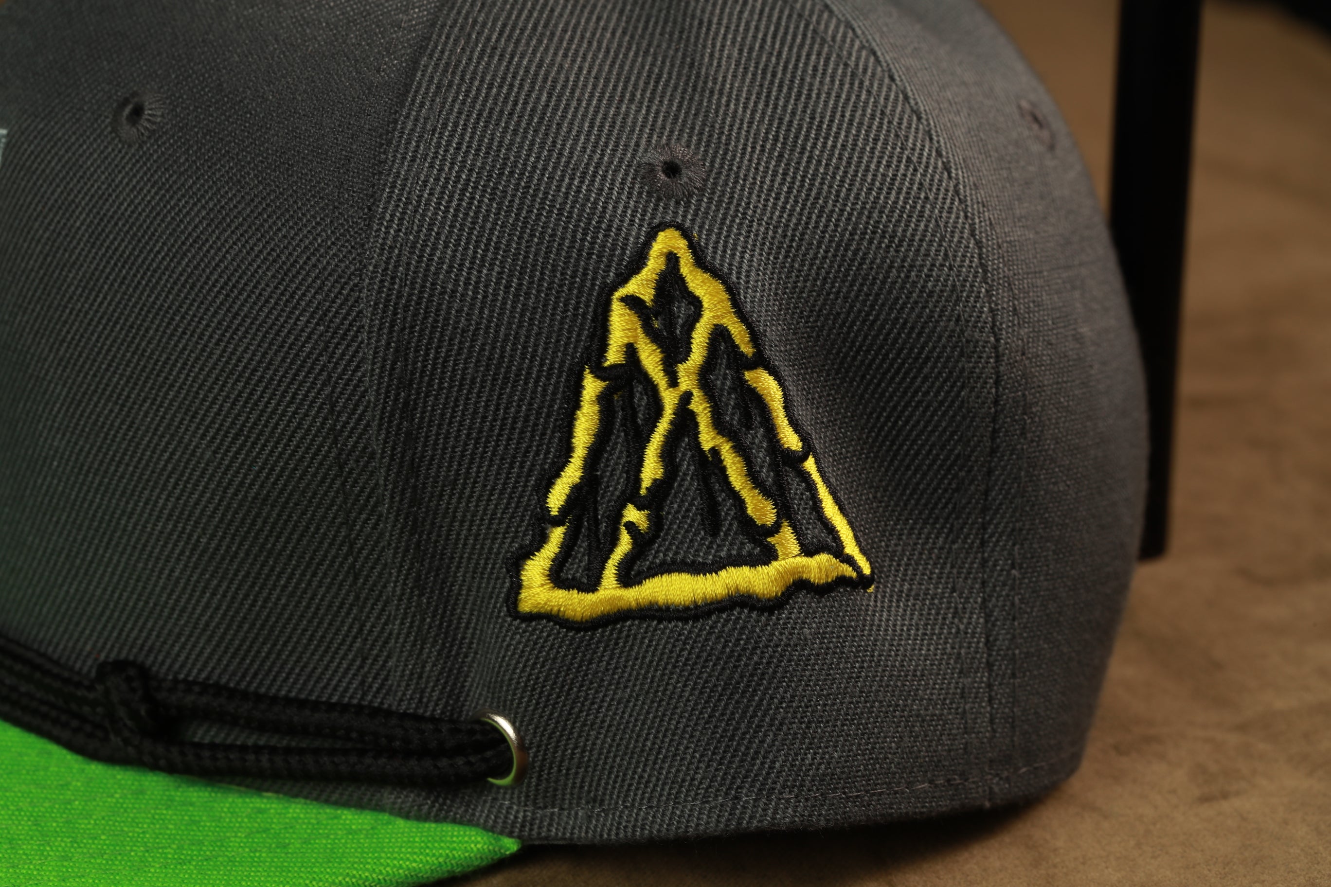 A close-up view of a gray baseball cap with a yellow triangle embroidered on the front.