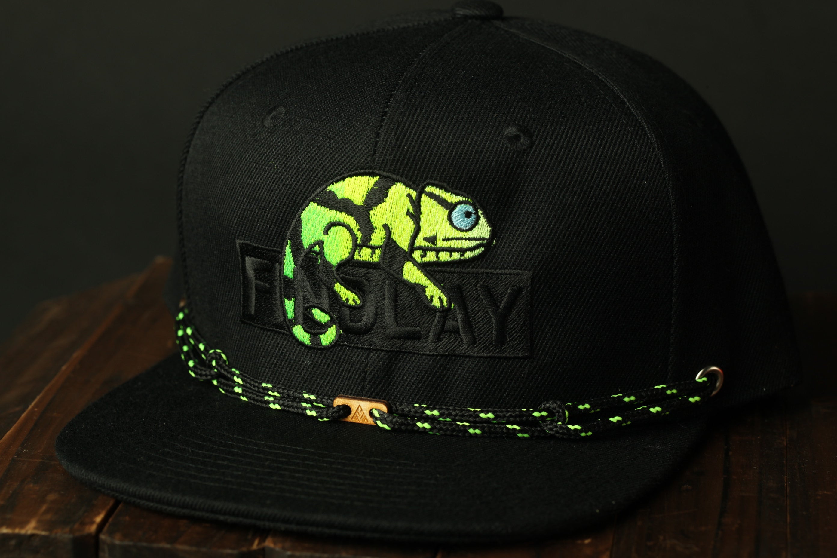 A black baseball cap with a green and black chameleon design and the word "FISH" printed on it.