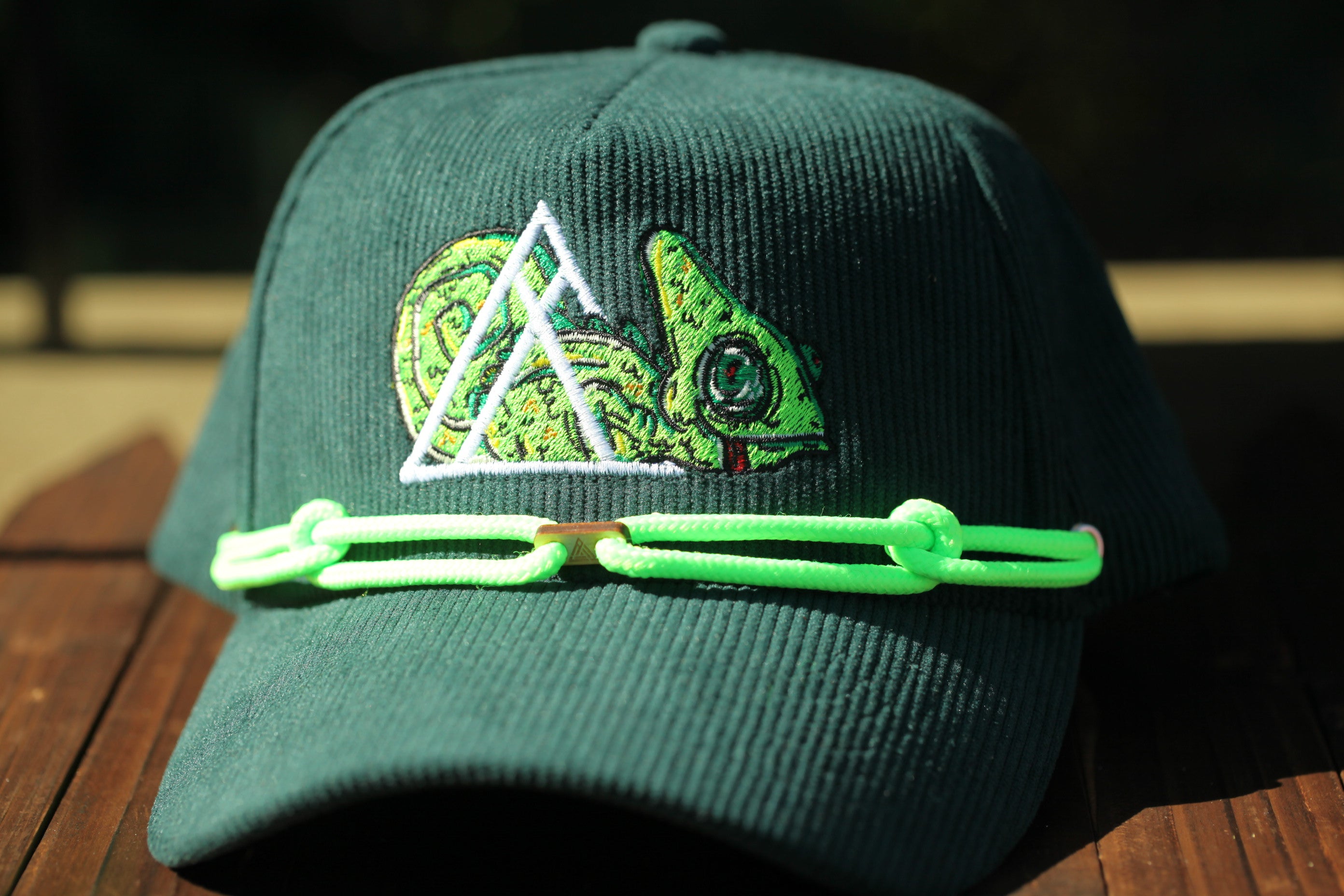 A green baseball cap with a chameleon design and a neon green string around the brim.
