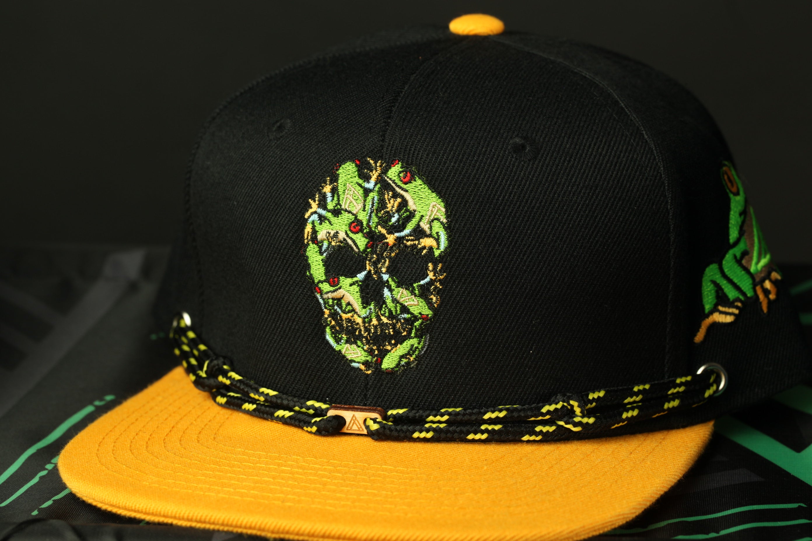 A black baseball cap with a yellow brim and a skull design on the front.