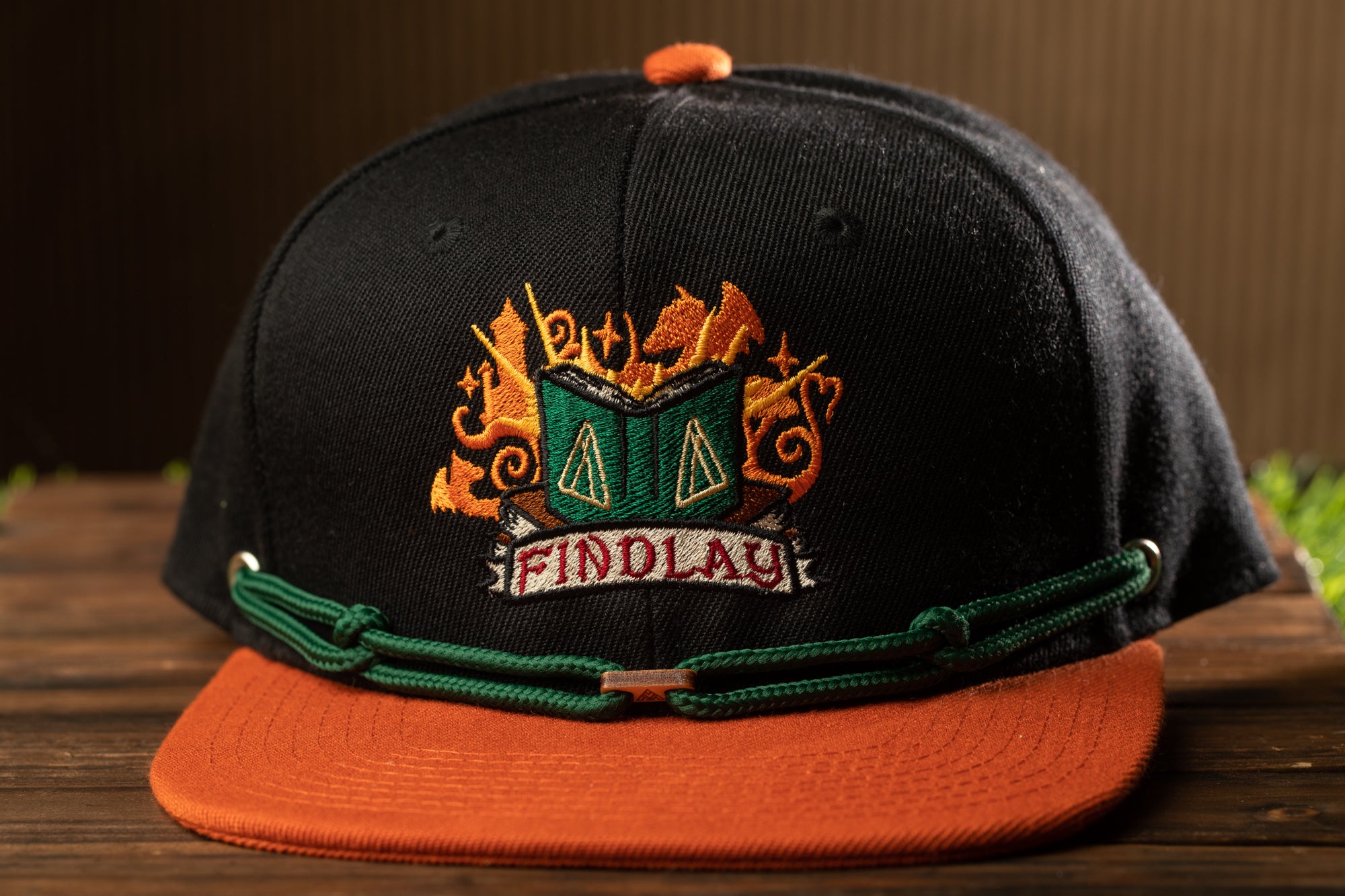 A black baseball cap with an orange brim and a green band, featuring an embroidered logo with flames and the word "FINDLAY" on it.