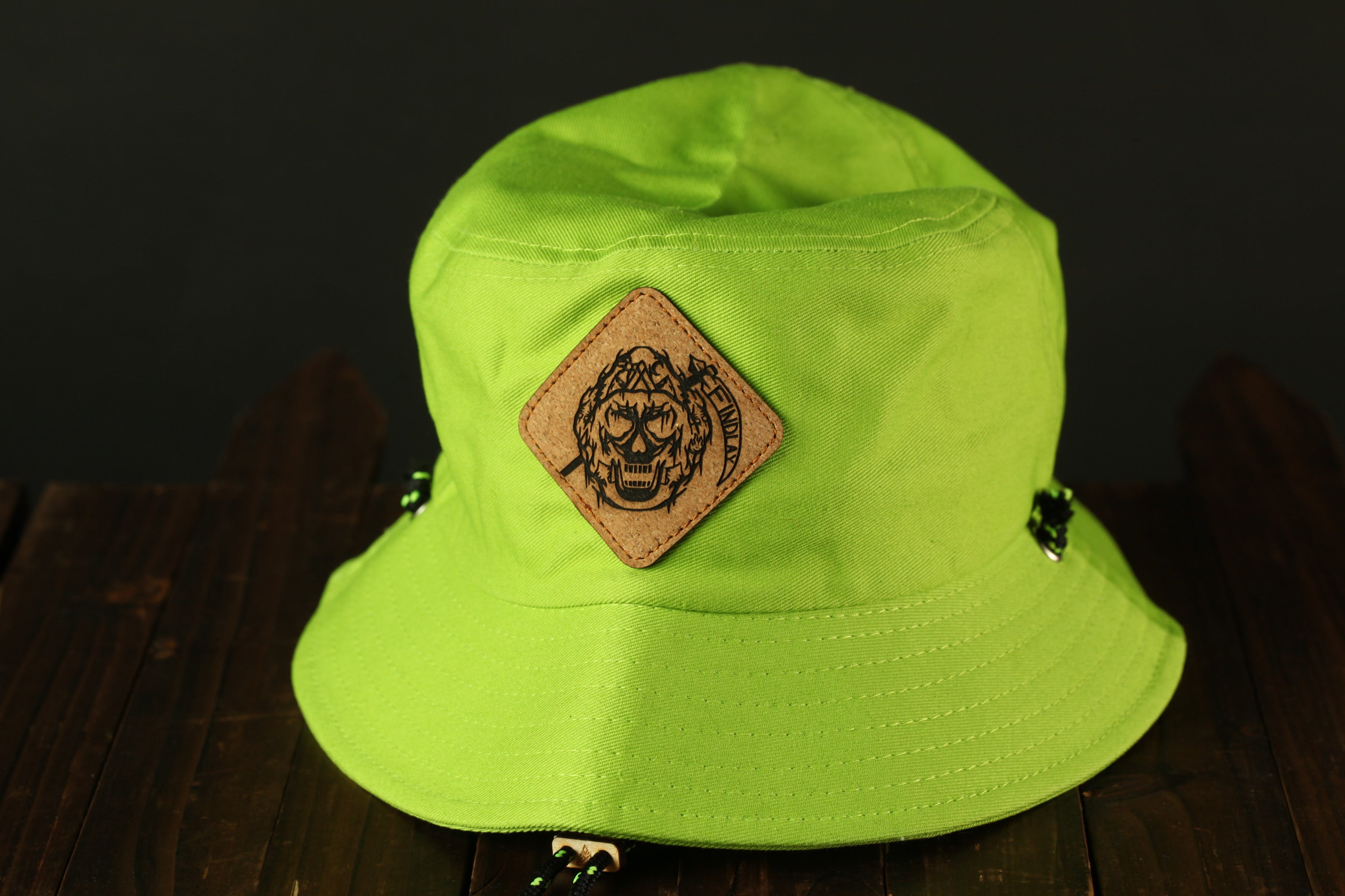 A bright green bucket hat with a brown patch featuring a skull design on the front.