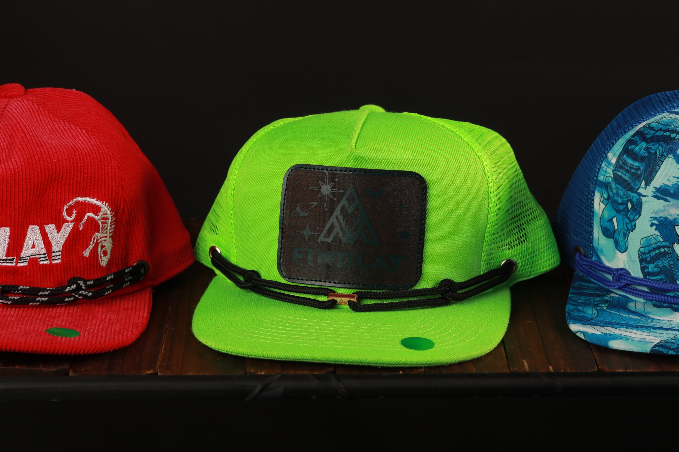 Three colorful baseball caps are displayed on a shelf, with the middle cap being neon green and the other two being red and blue.