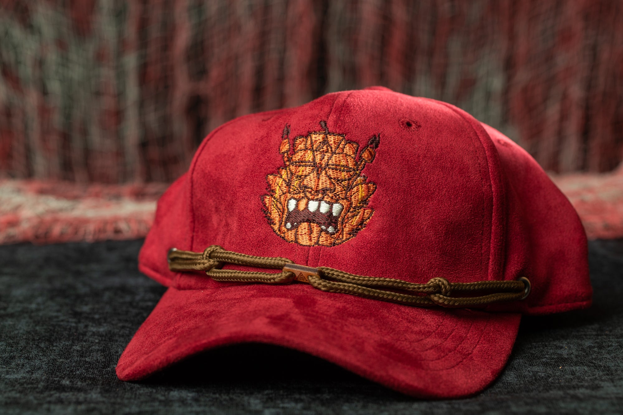 A red baseball cap with a brown rope detail and an embroidered design on the front.