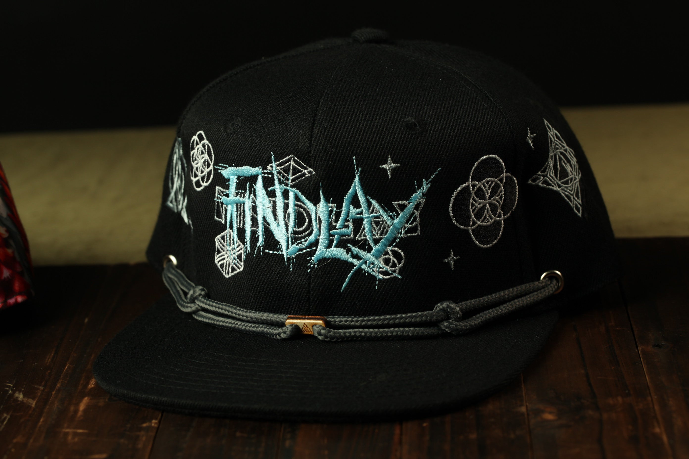 A black baseball cap with the word "FINDLAY" embroidered on it, sitting on a wooden surface.