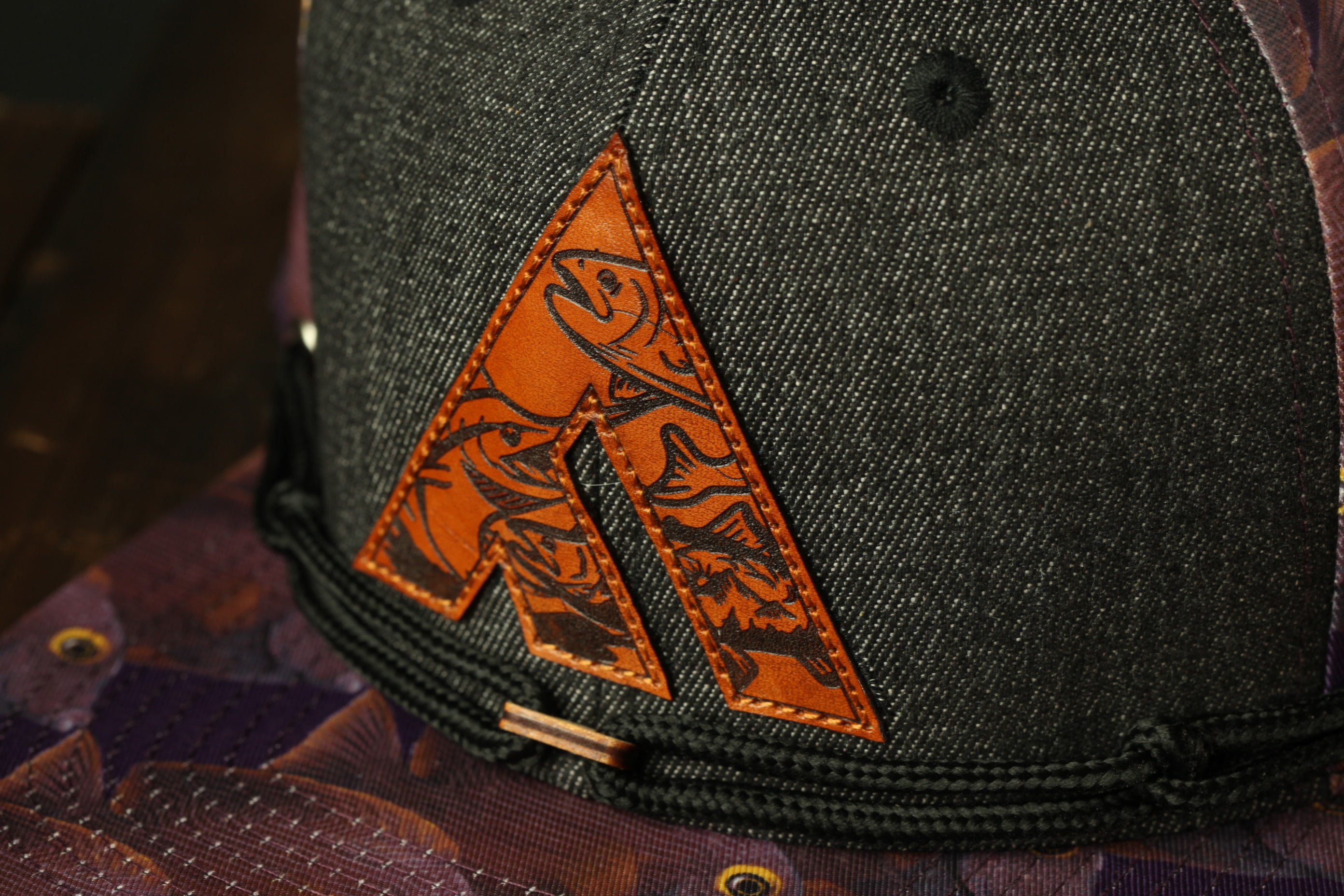 A close-up view of a black baseball cap with a distinctive orange and black logo on the front.
