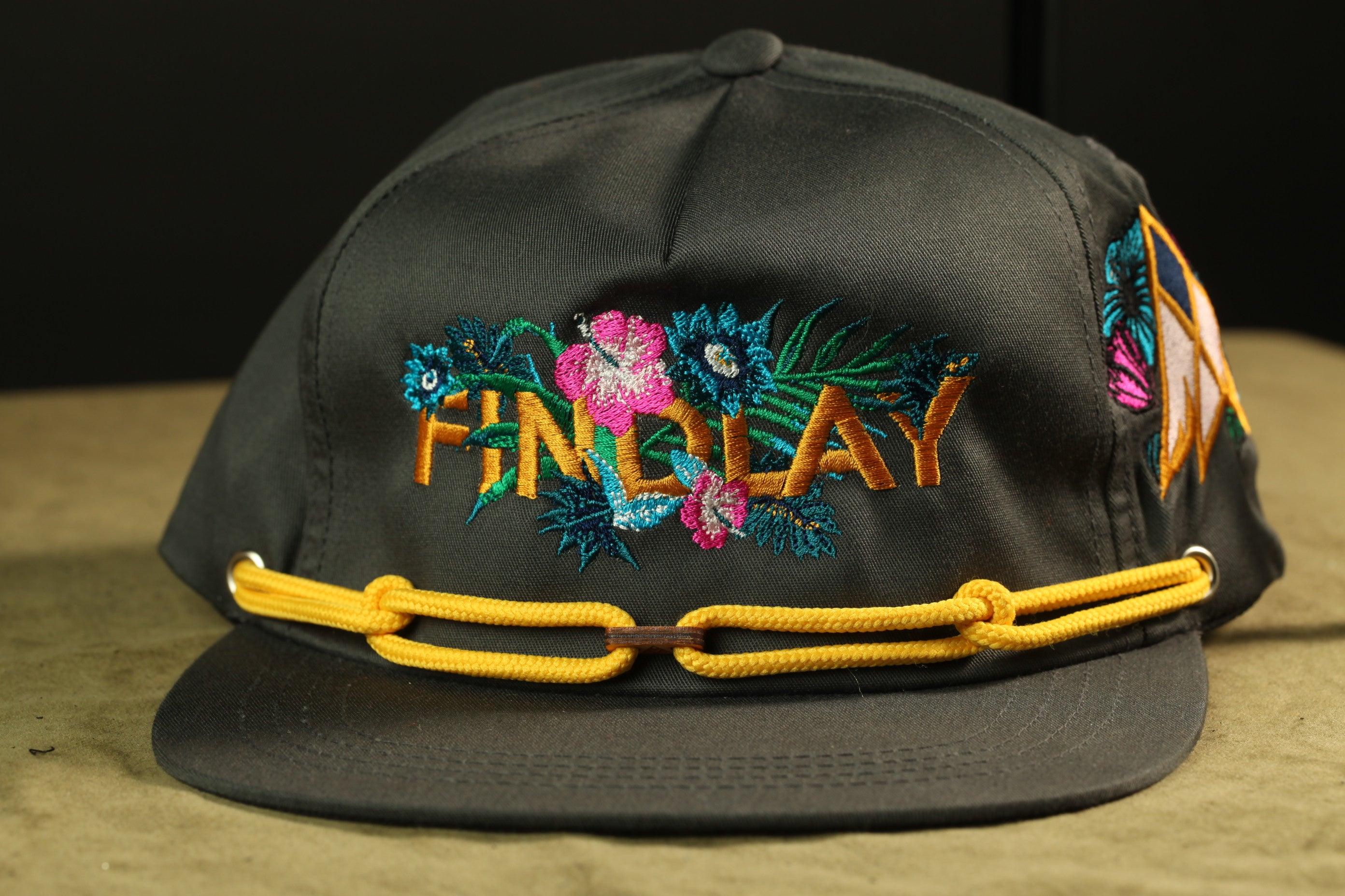 A black baseball cap with colorful floral embroidery and a yellow chain strap.