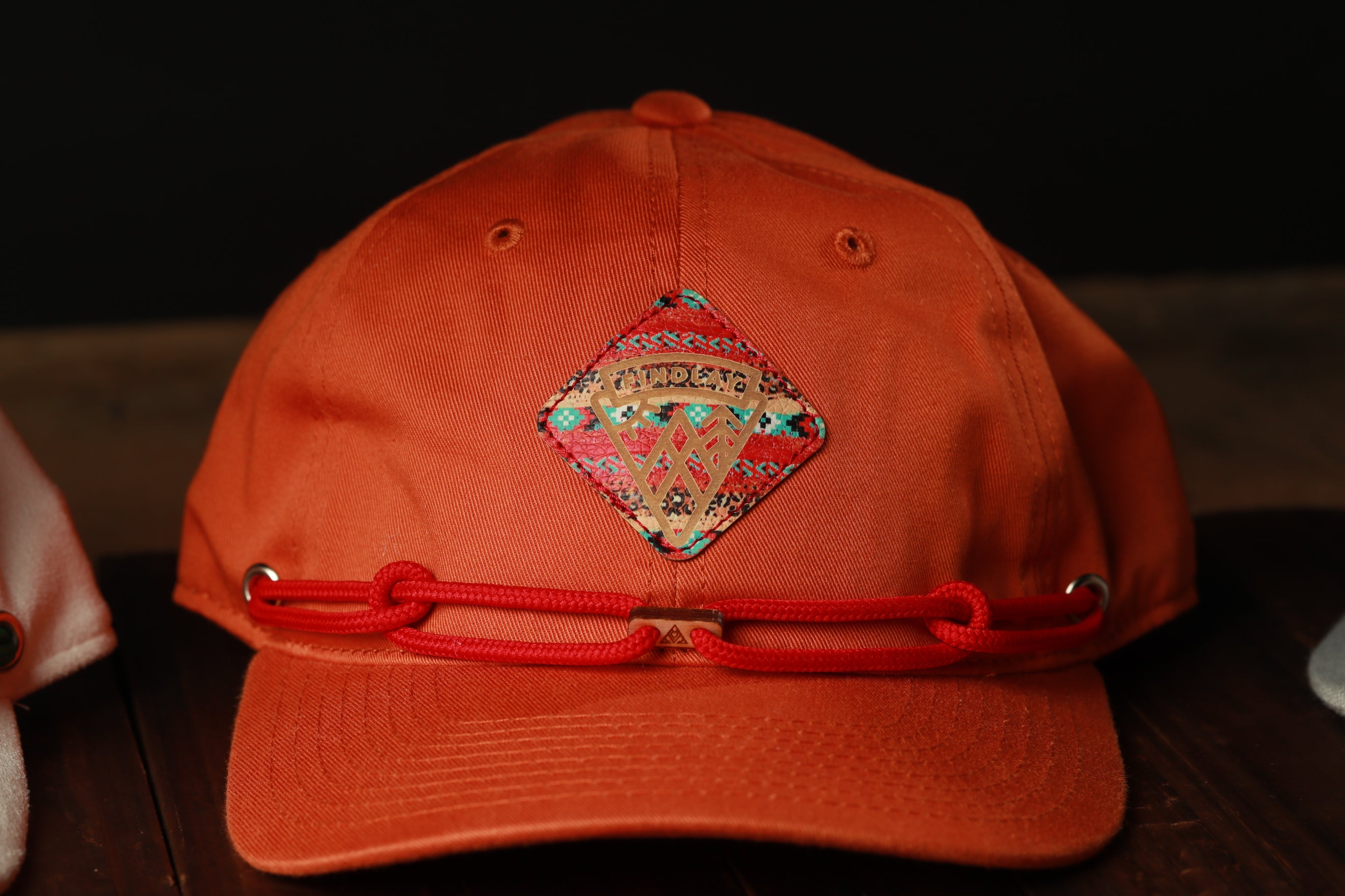 An orange baseball cap with a red strap and a decorative patch on the front.
