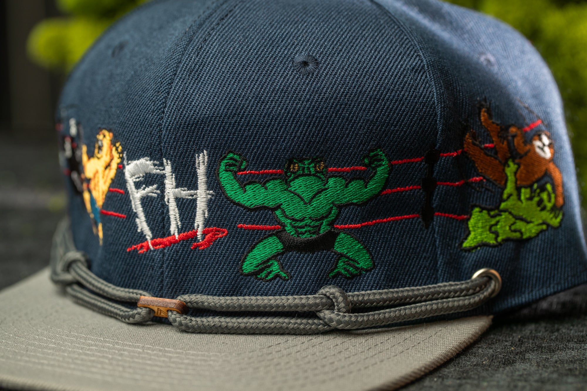 A close-up of a baseball cap with various cartoon-style characters and text embroidered on it.