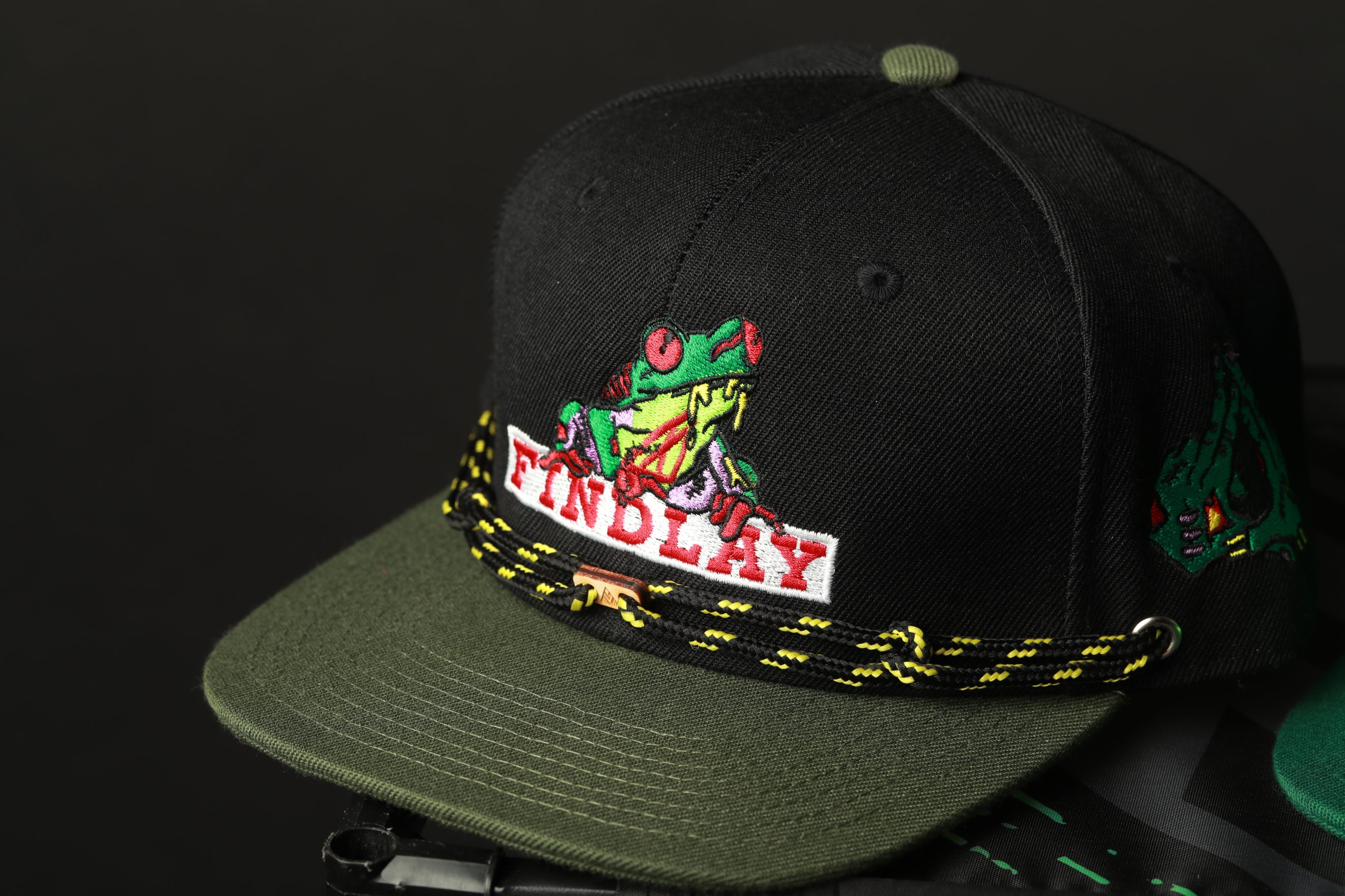 A black baseball cap with a colorful frog design and the word "FINDlay" printed on it.
