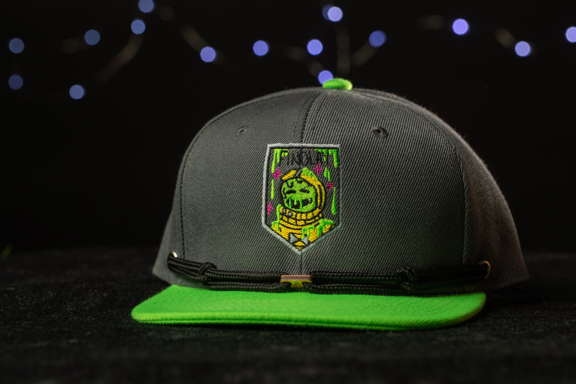A gray baseball cap with a green brim and a green and yellow patch on the front, featuring a skull and crossbones design.