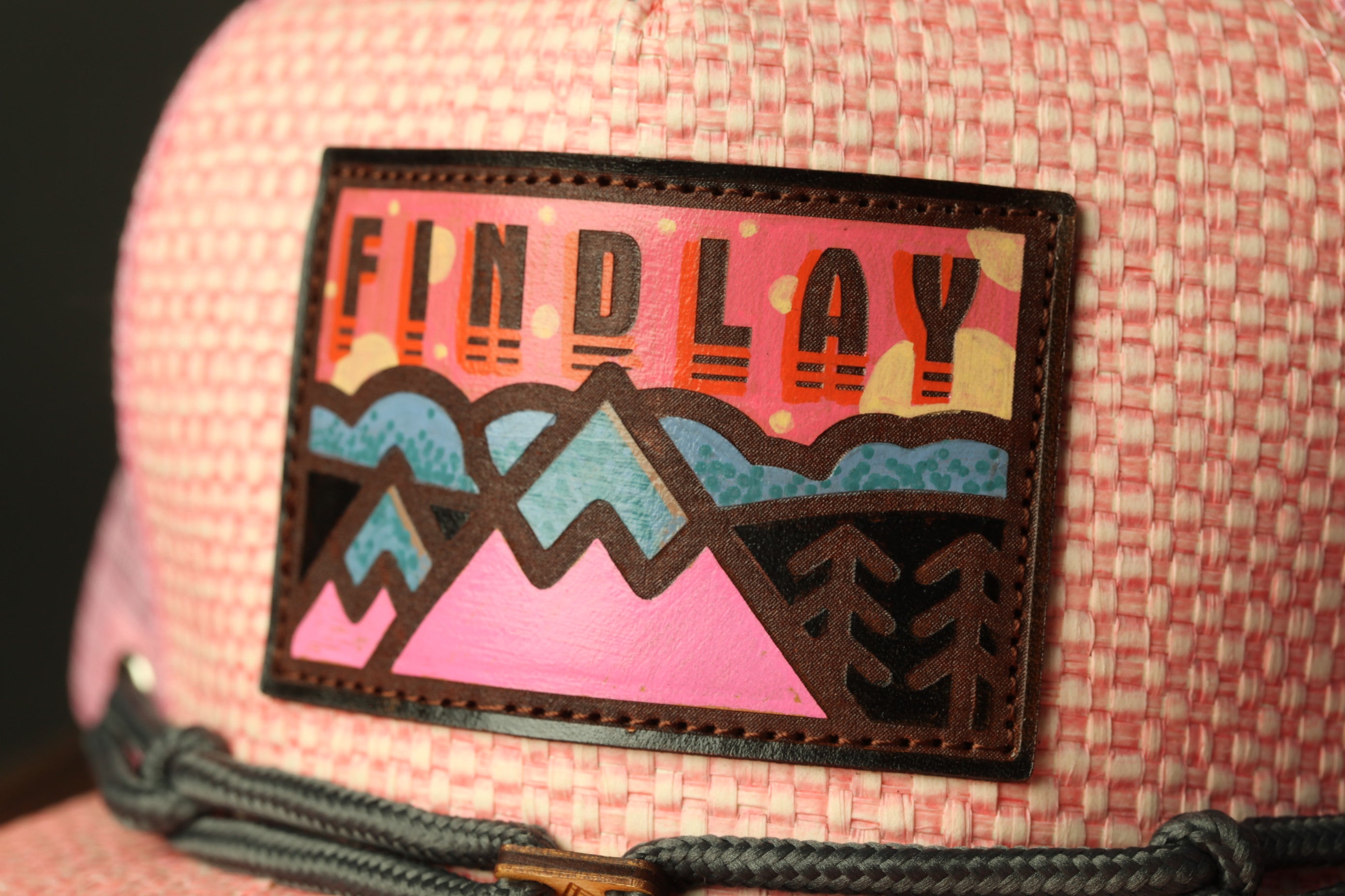 A close-up of a pink and white woven hat with a patch on the front that says "FIND LAY".