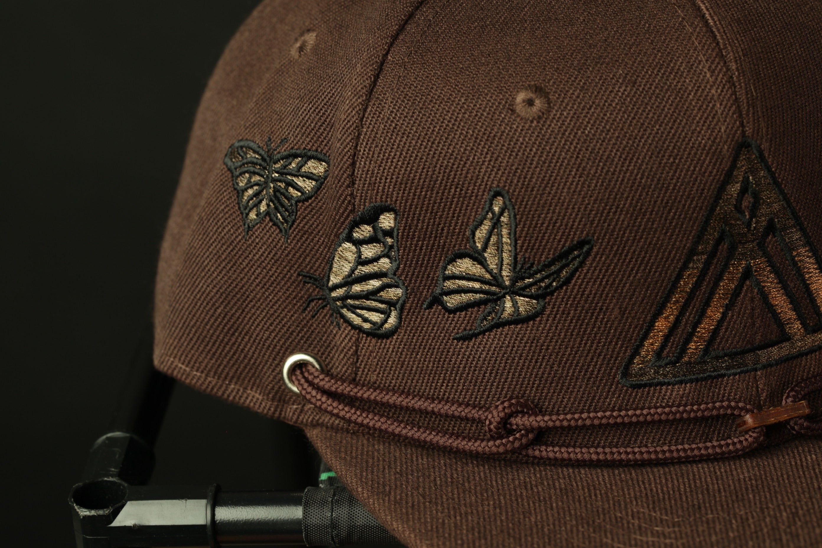 A close-up view of a brown baseball cap with a butterfly design on the front.