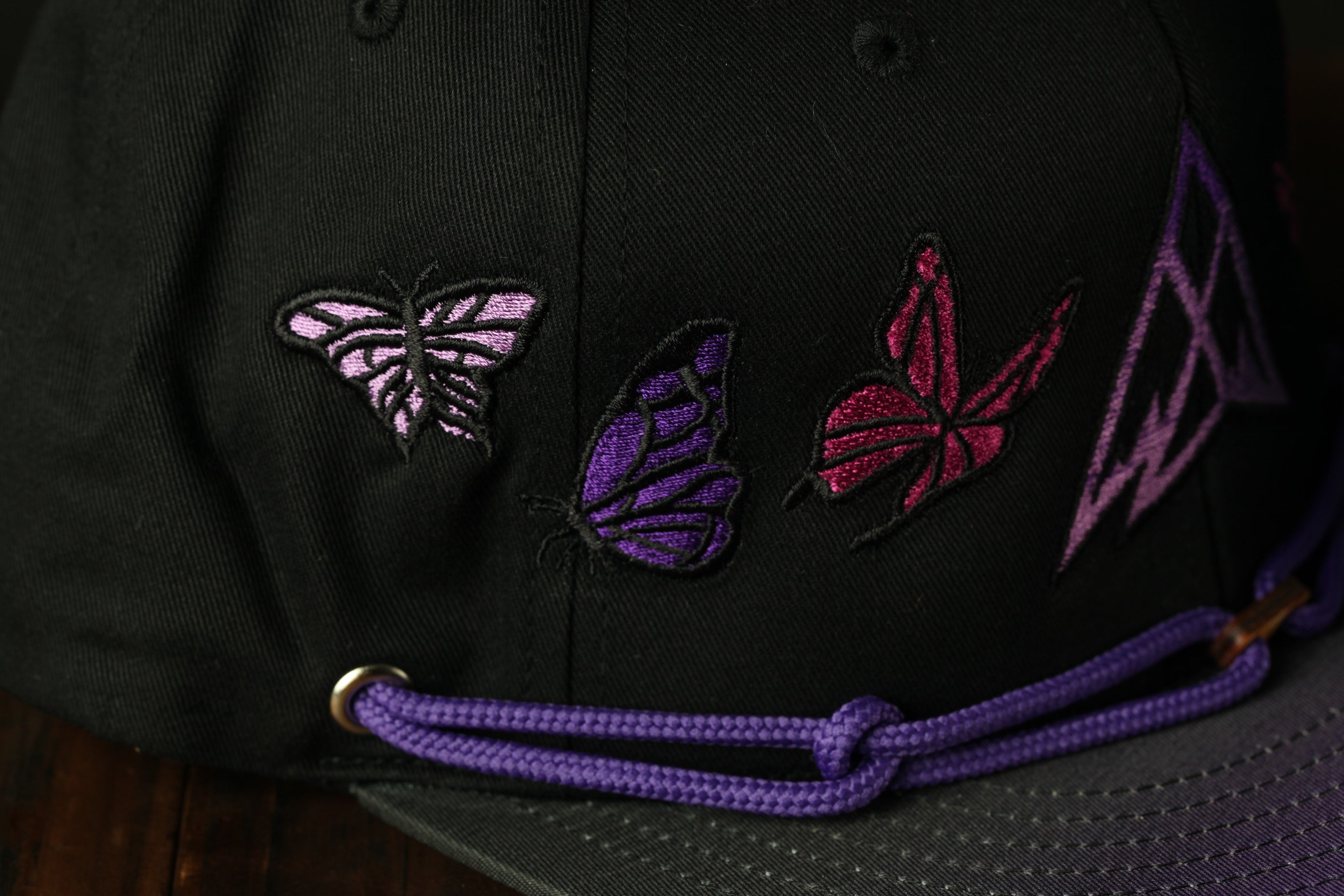 A close-up view of a black baseball cap with purple and pink butterfly embroidered designs on the front.