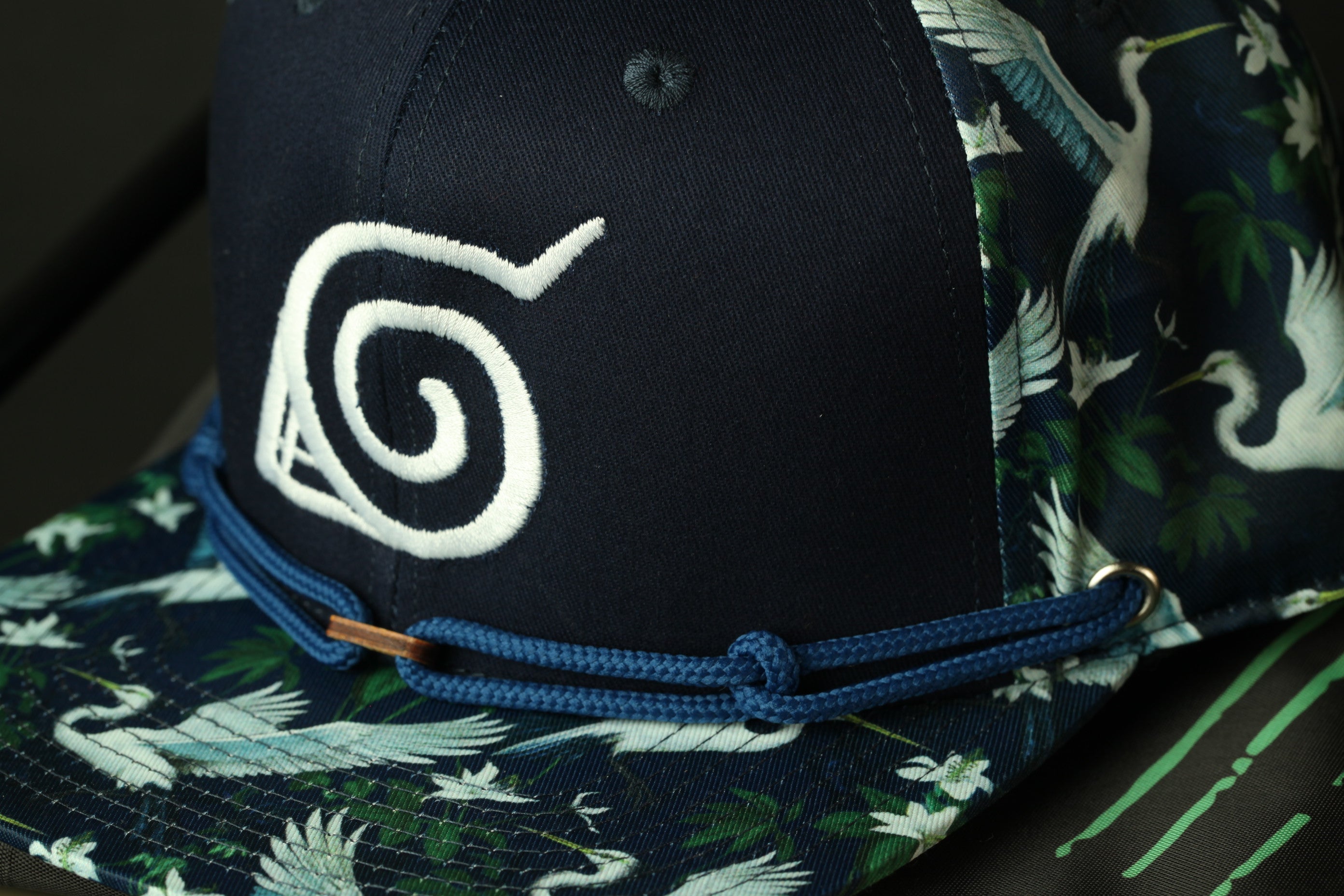 A close-up view of a black baseball cap with a pattern of white and green birds on the front.