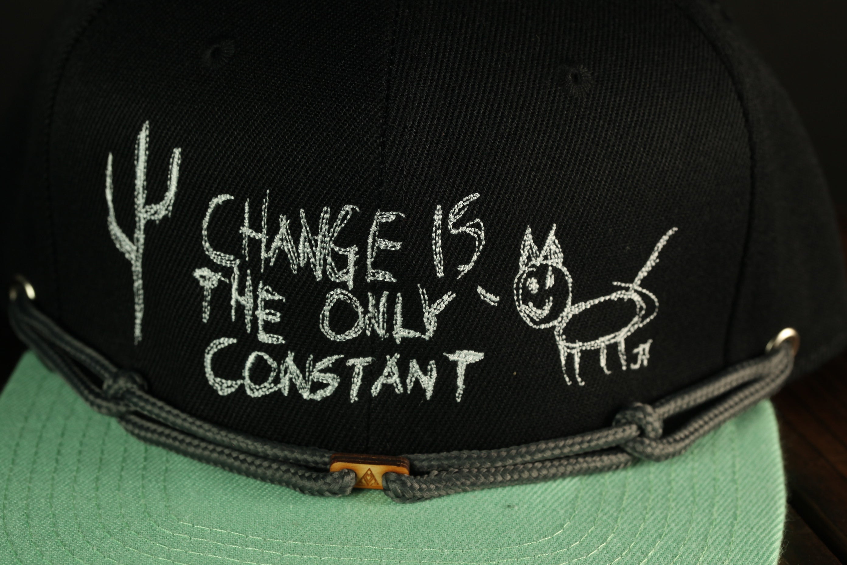 A black baseball cap with white text and a drawing on it.