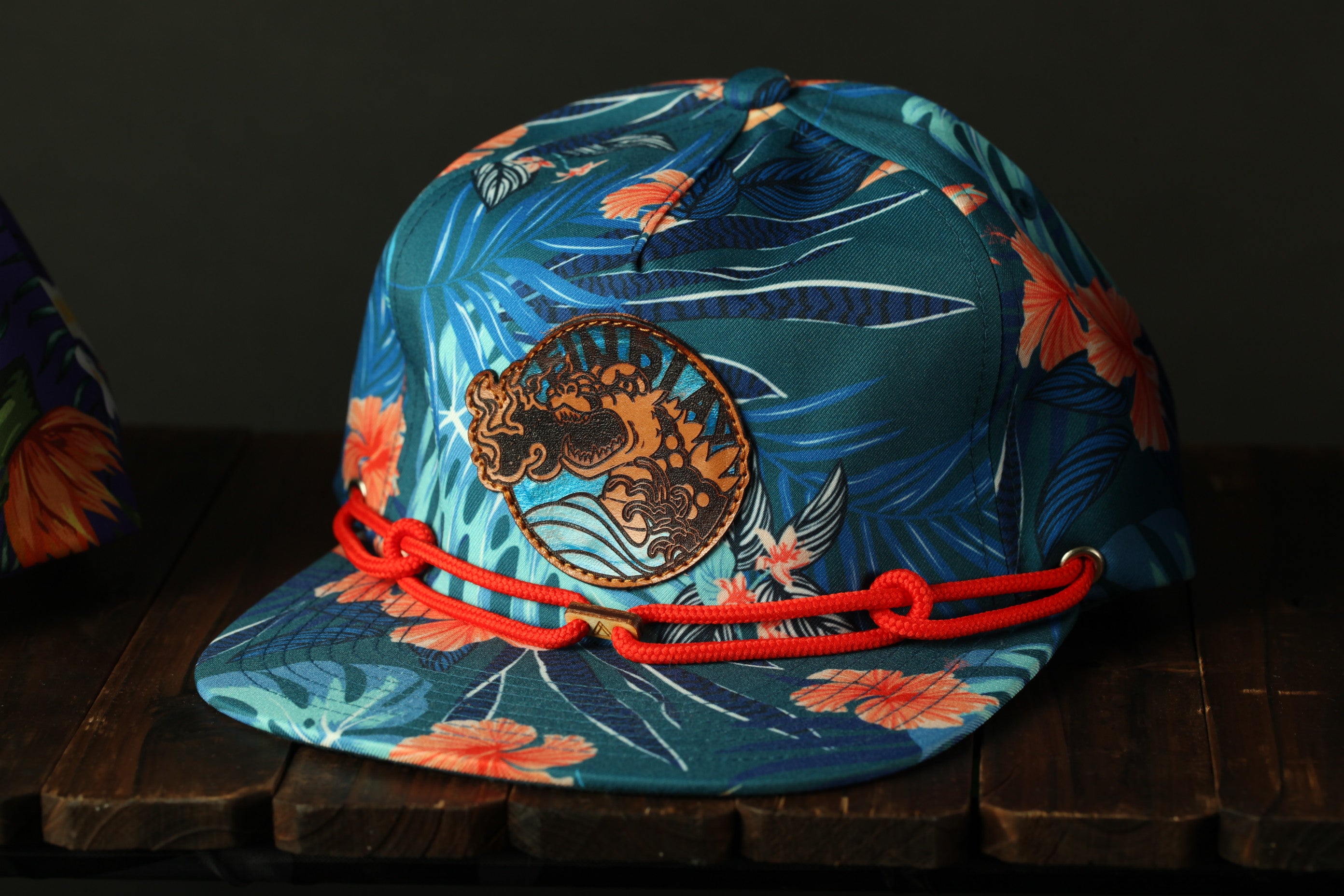 A colorful floral patterned baseball cap with a red string around the brim, placed on a wooden surface.