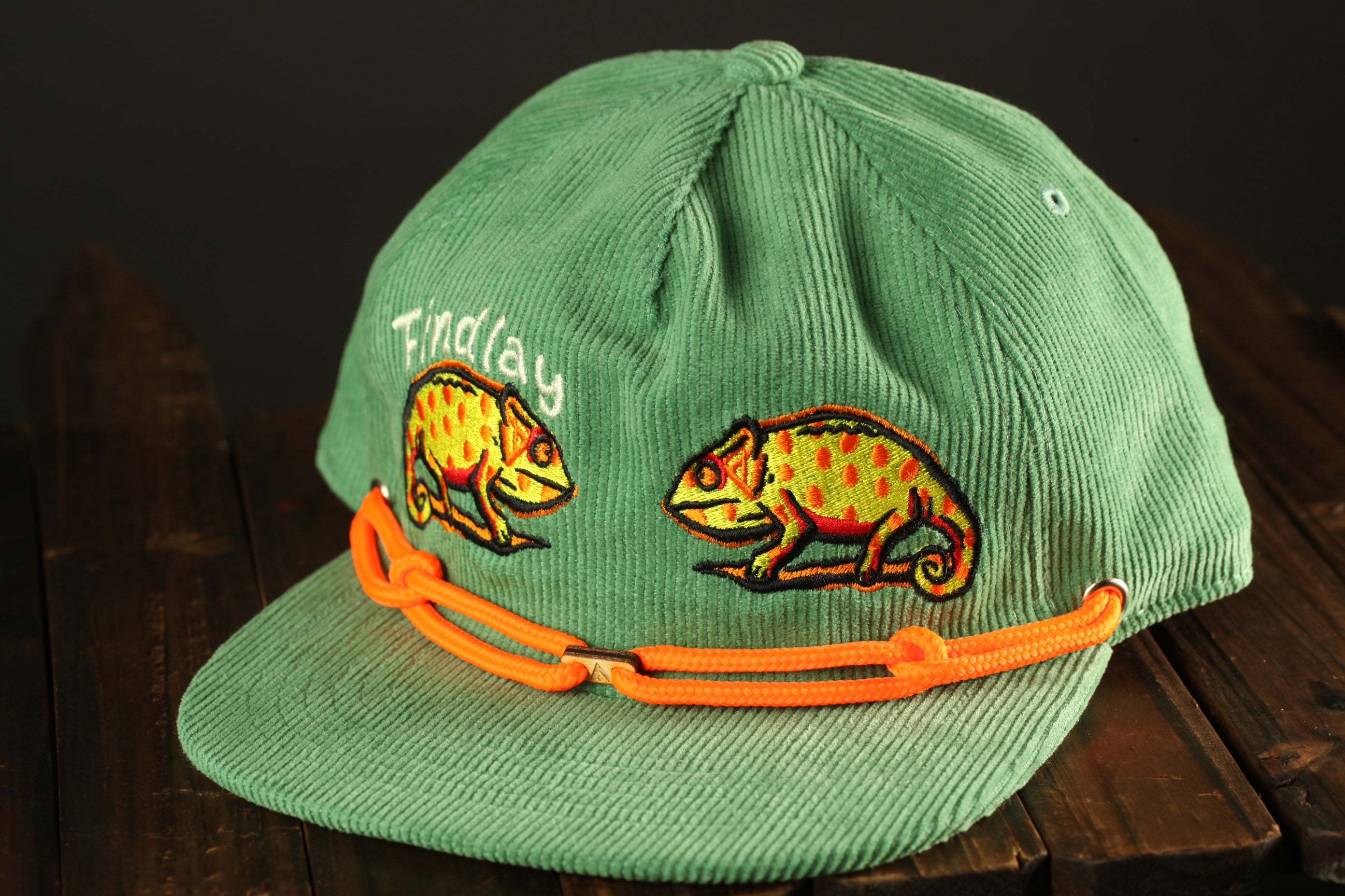 A green baseball cap with orange straps and two chameleon designs on the front.