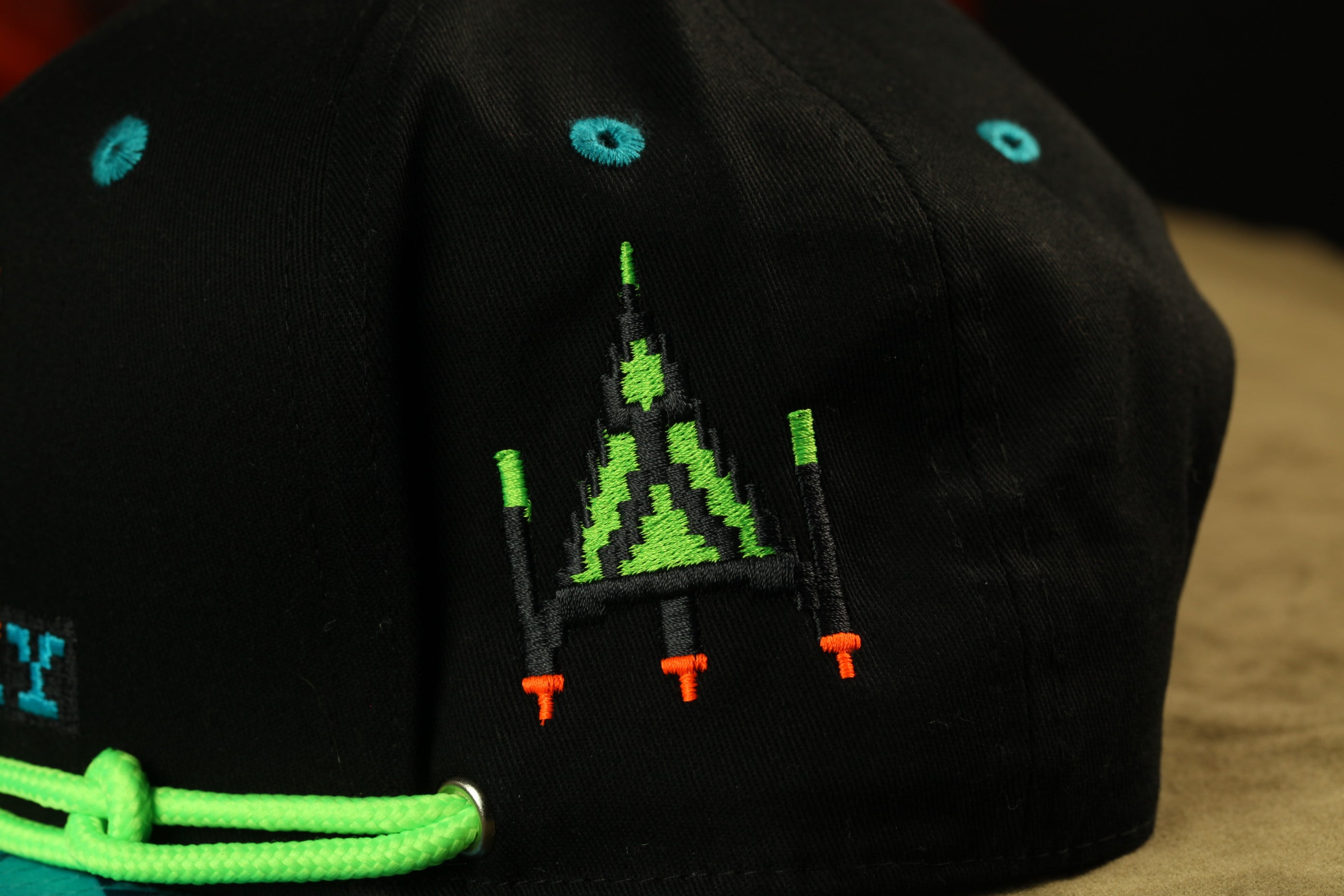 A close-up view of a black baseball cap with a green and orange pixelated design on the front.