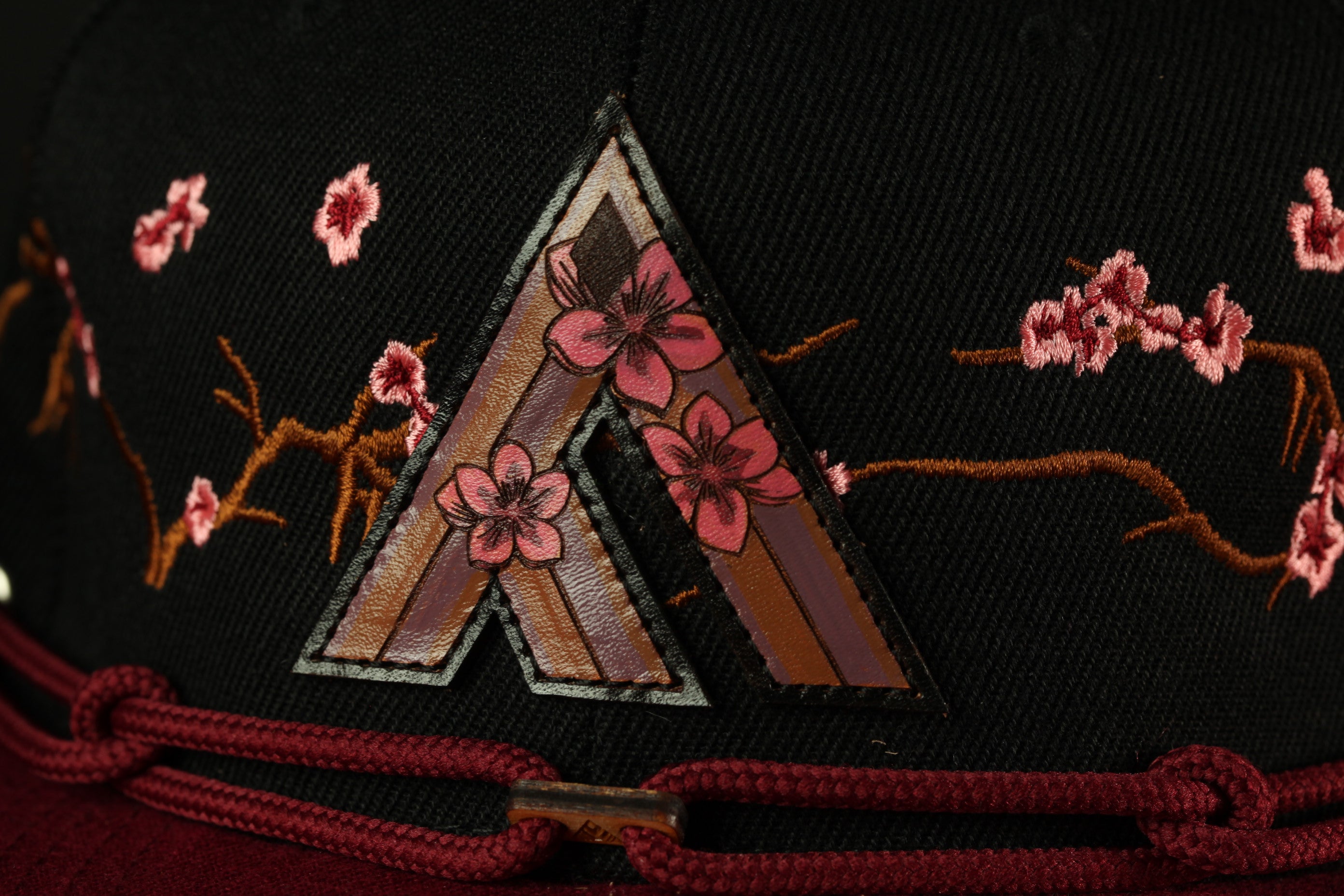 A close-up view of a black baseball cap with a decorative floral pattern on the front.