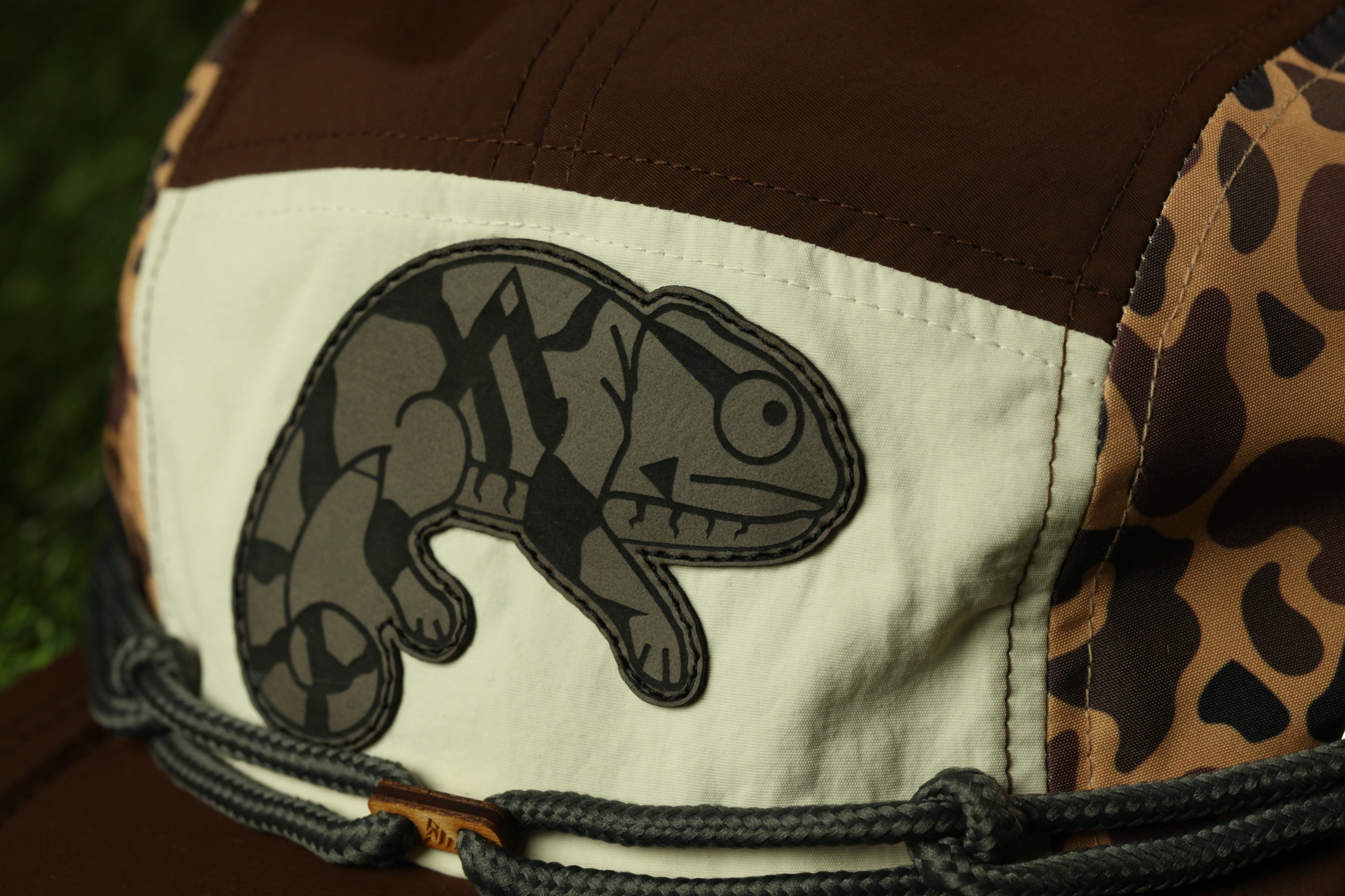 A close-up view of a brown and white hat with a black and white chameleon design on the front.