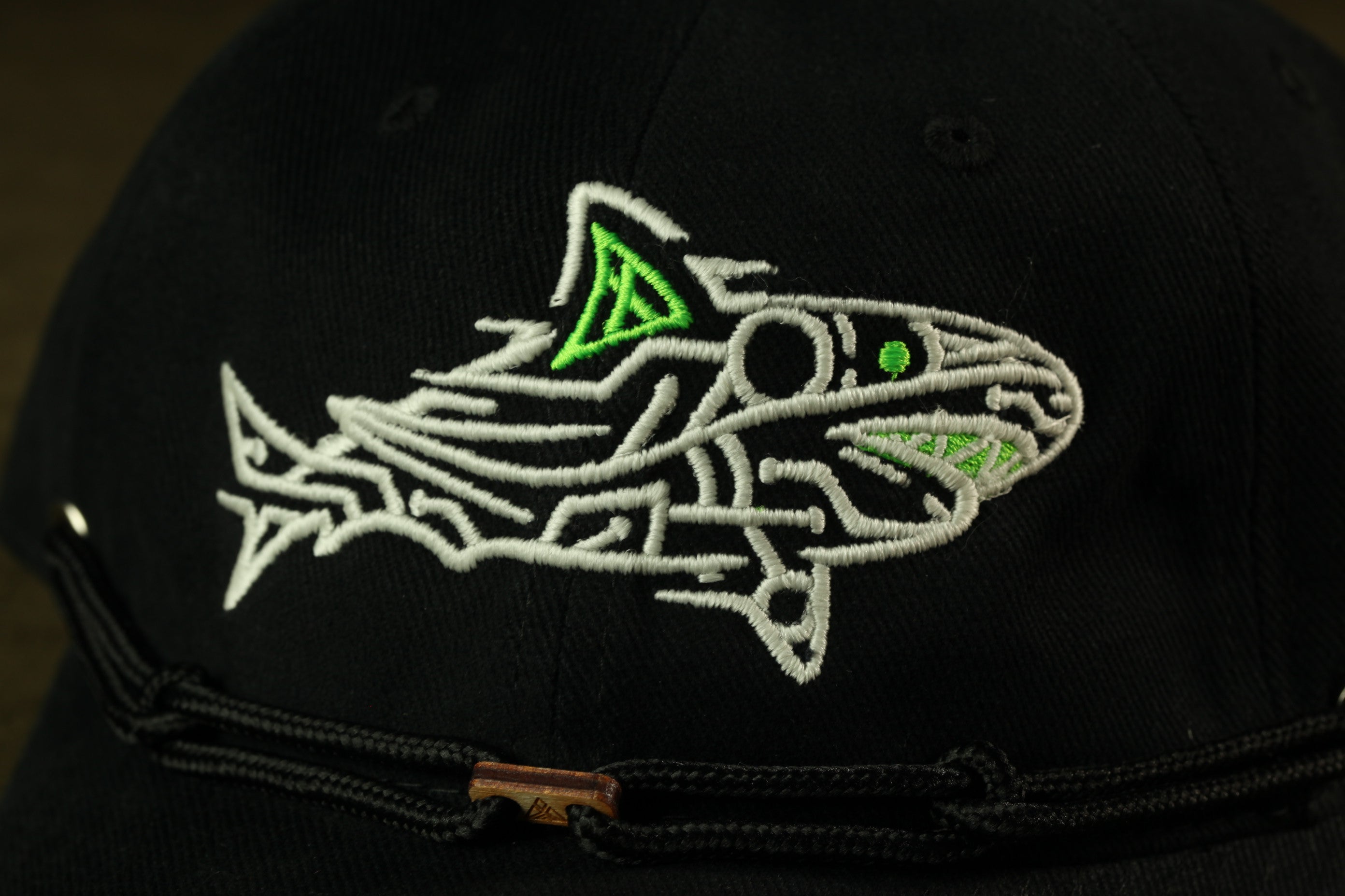 A close-up view of a black baseball cap with a white embroidered shark design on the front.